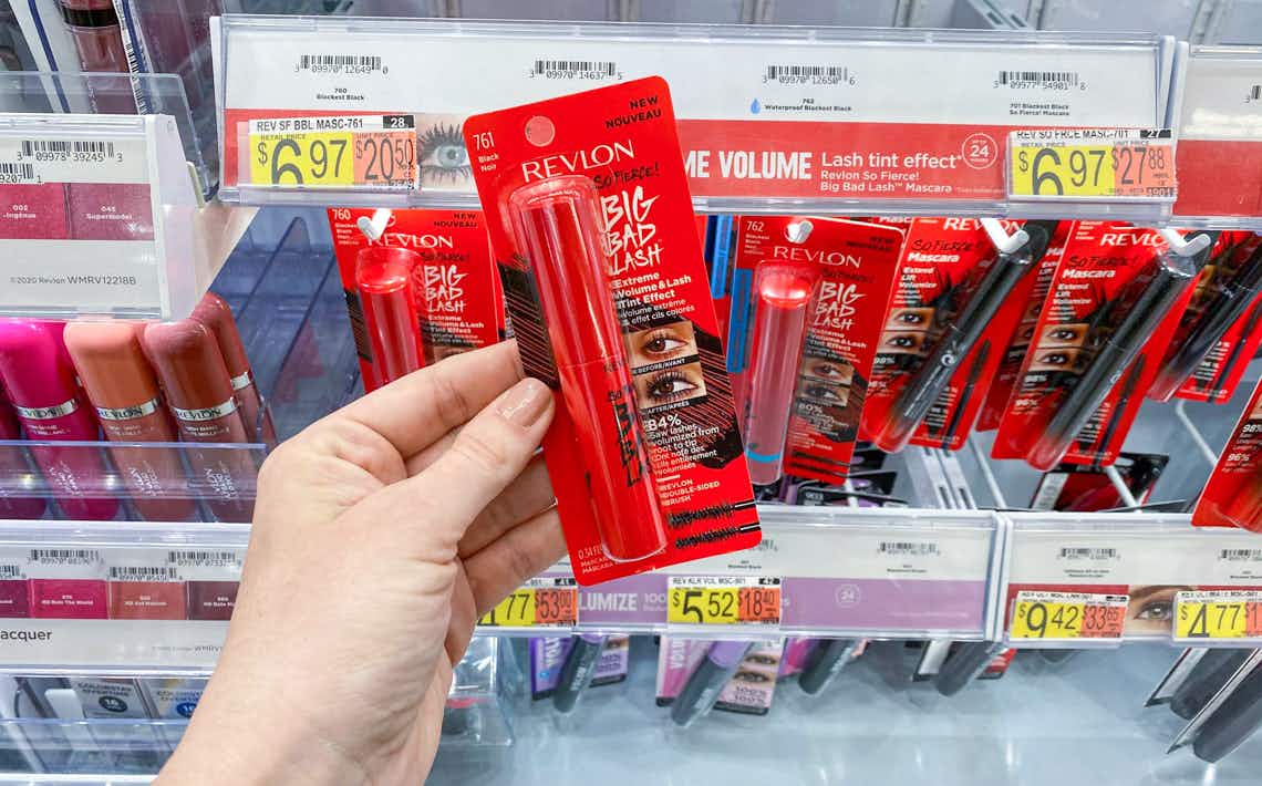 left hand holding bright red revlon so fierce mascara package in front of other packs and walmart price tag