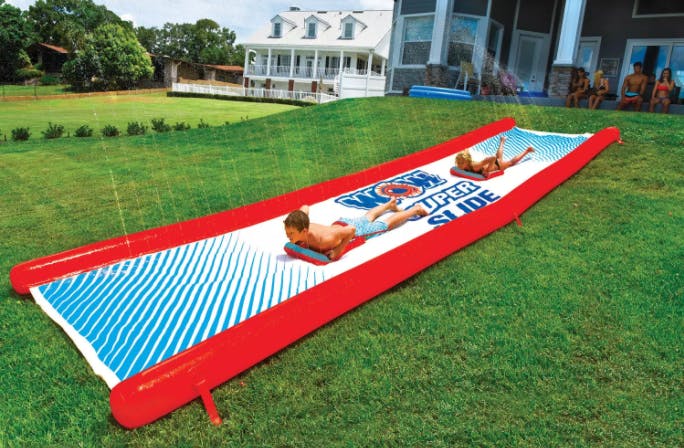 Kids playing on a Slip n Slide outside on the grass.
