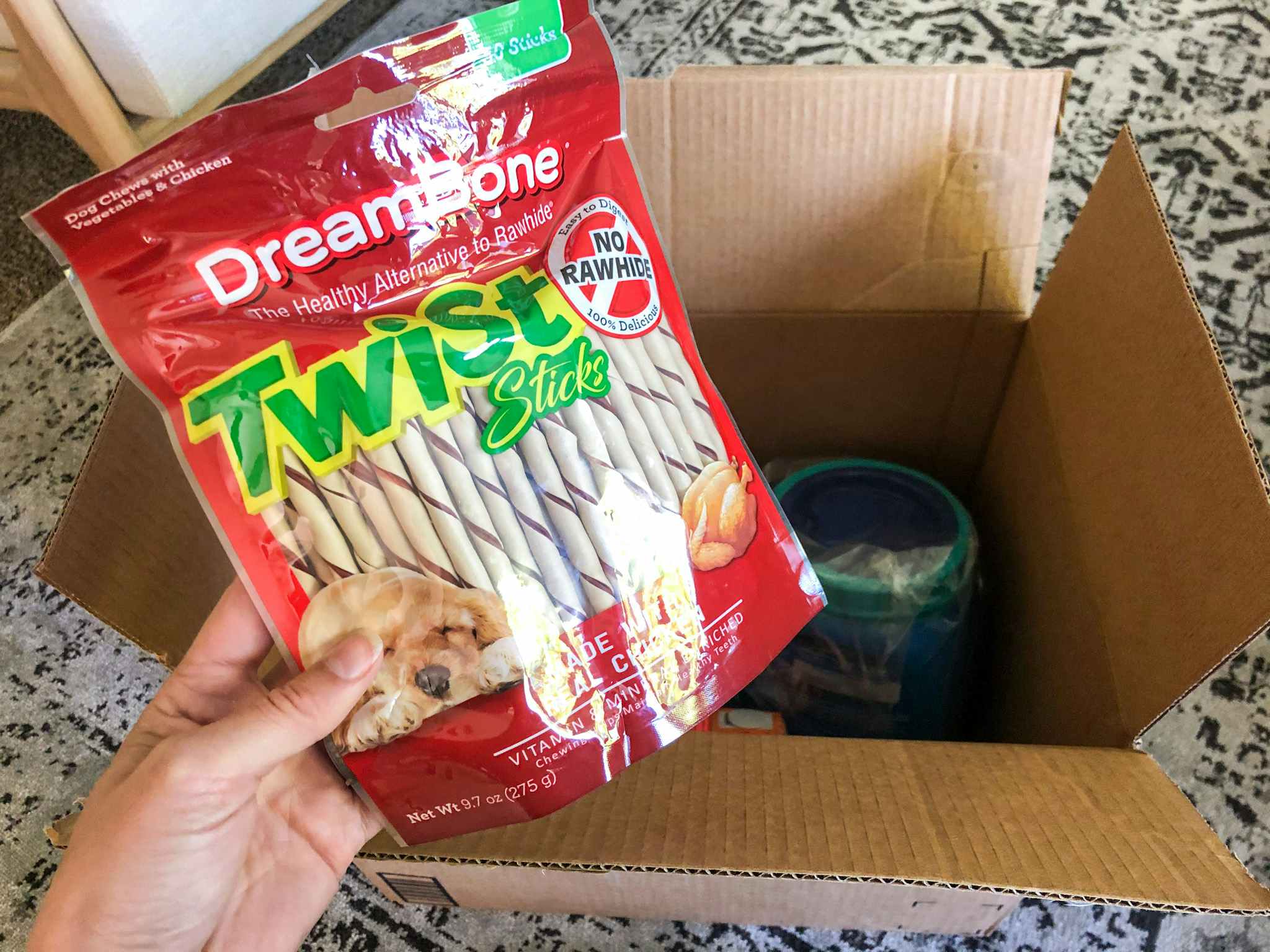 A hand holding Dreambone Twist Sticks near an open delivery box.