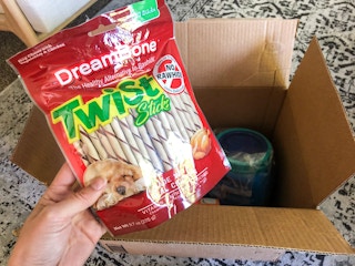 A hand holding Dreambone Twist Sticks near an open delivery box.