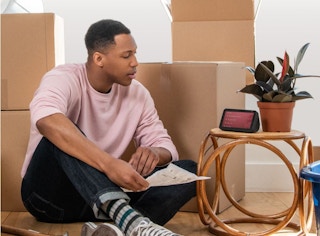 A man sitting near boxes and looking at his Echo Show 5