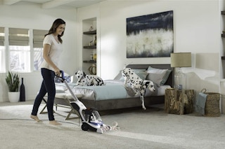 A woman vacuuming her carpet in her bedroom