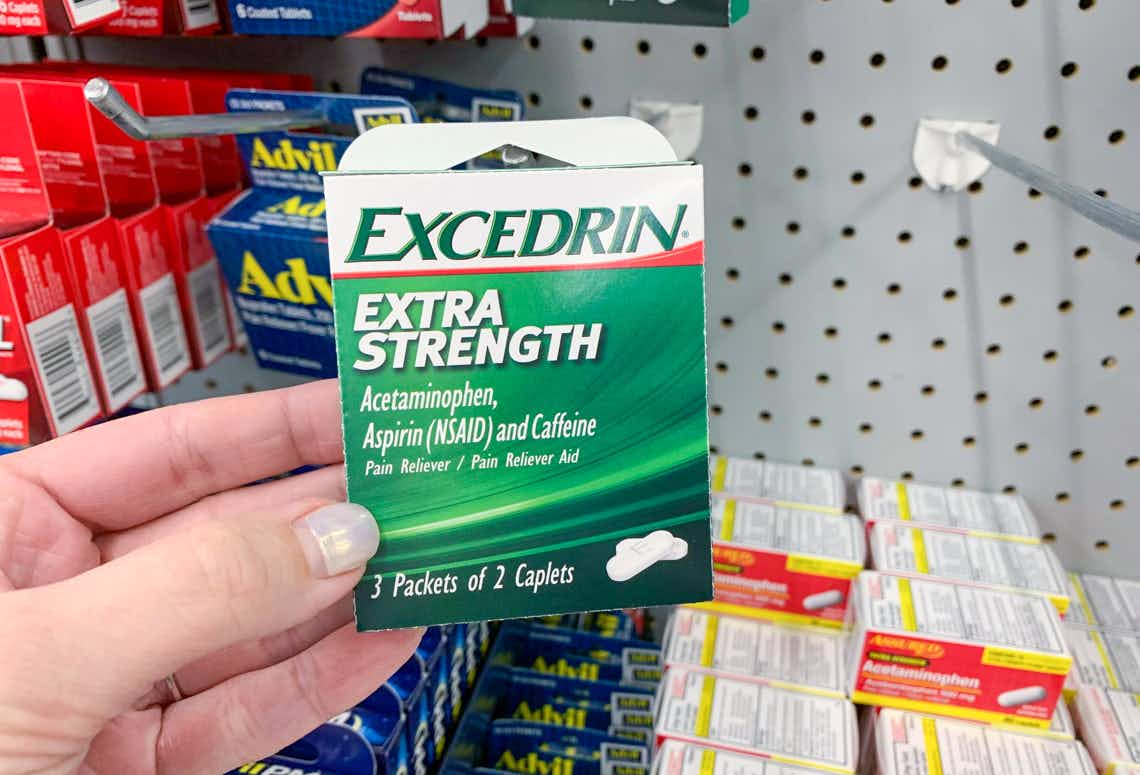 hand holding small green and white box of excedrin extra strength tablets in front o other pain relievers