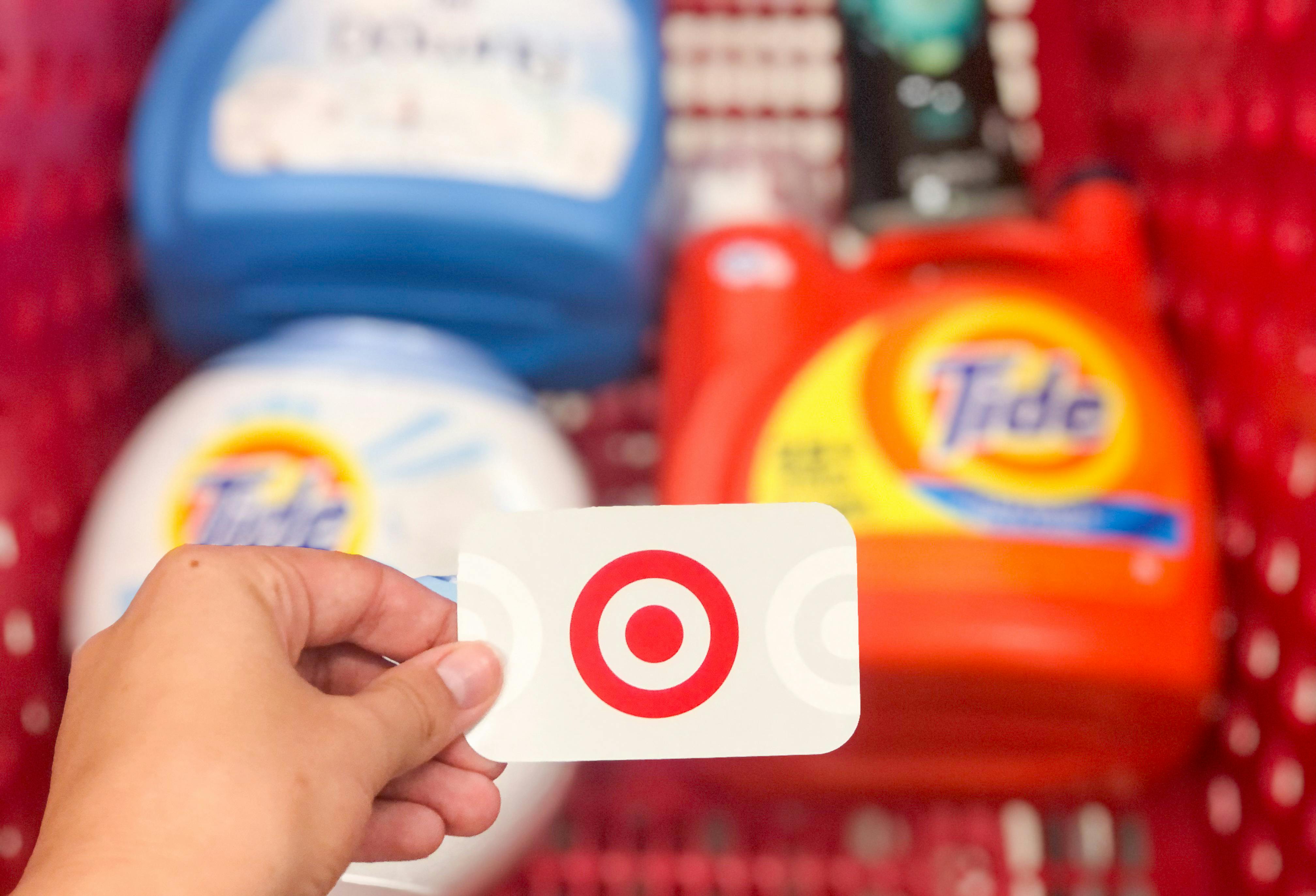 earn free gift cards - A person holding gift card over the top of a shopping cart that has bottles of laundry detergent