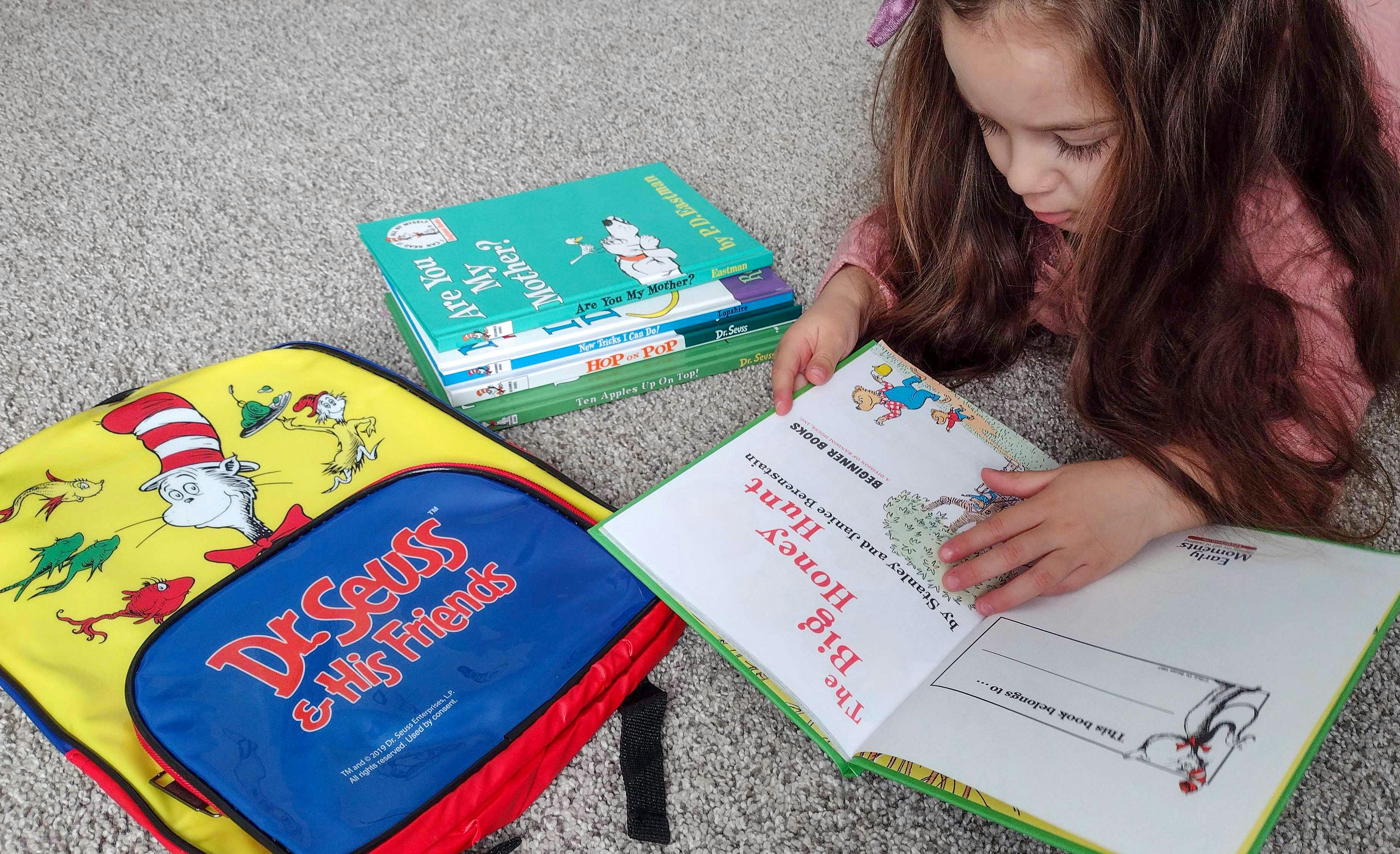 A child laying on the floor reading The Big Honey Hunt next to some more Dr. Seuss books and a Dr. Seuss backpack.