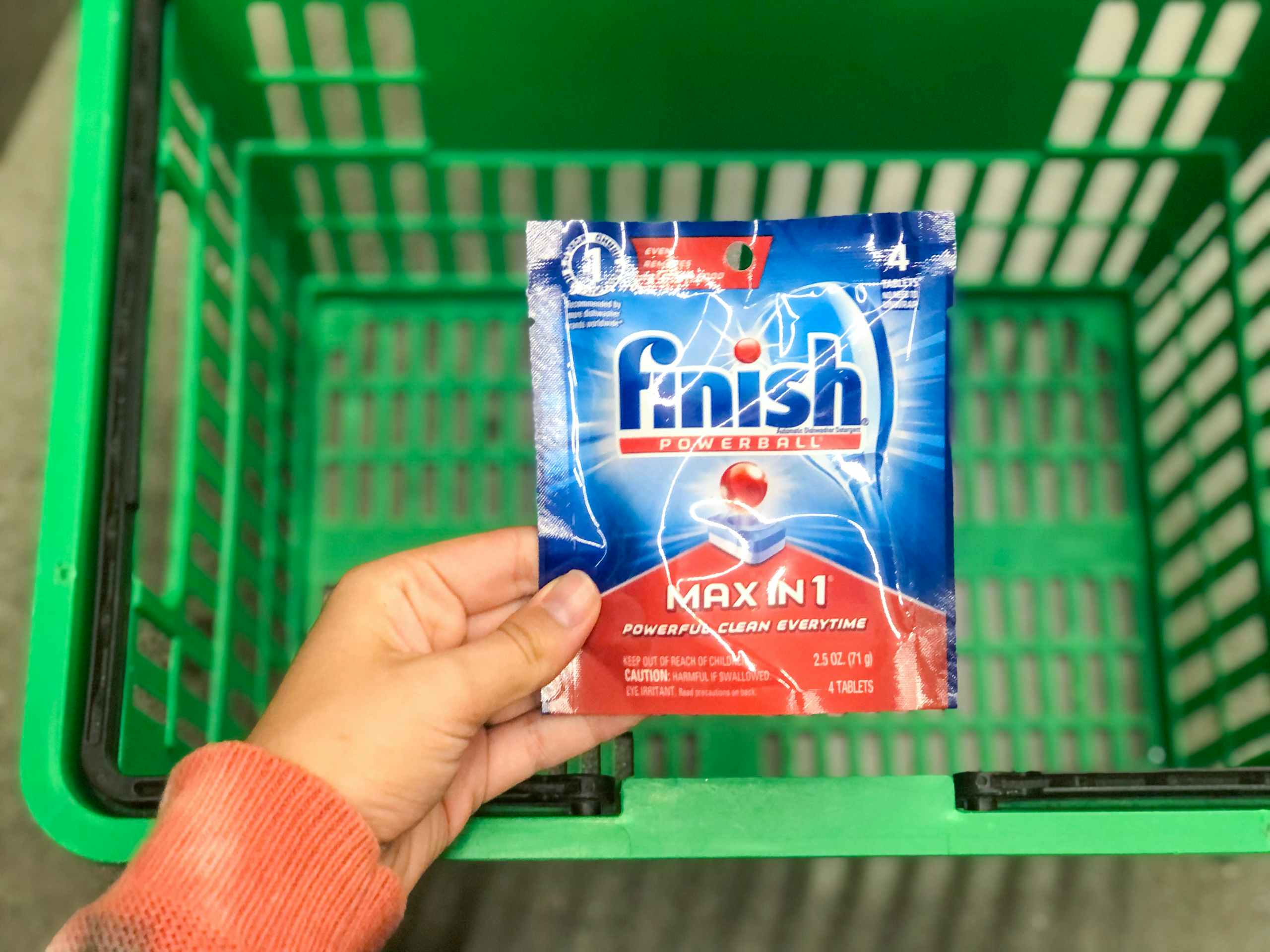 hand holding small pack of Finish dish detergent over store basket on the ground