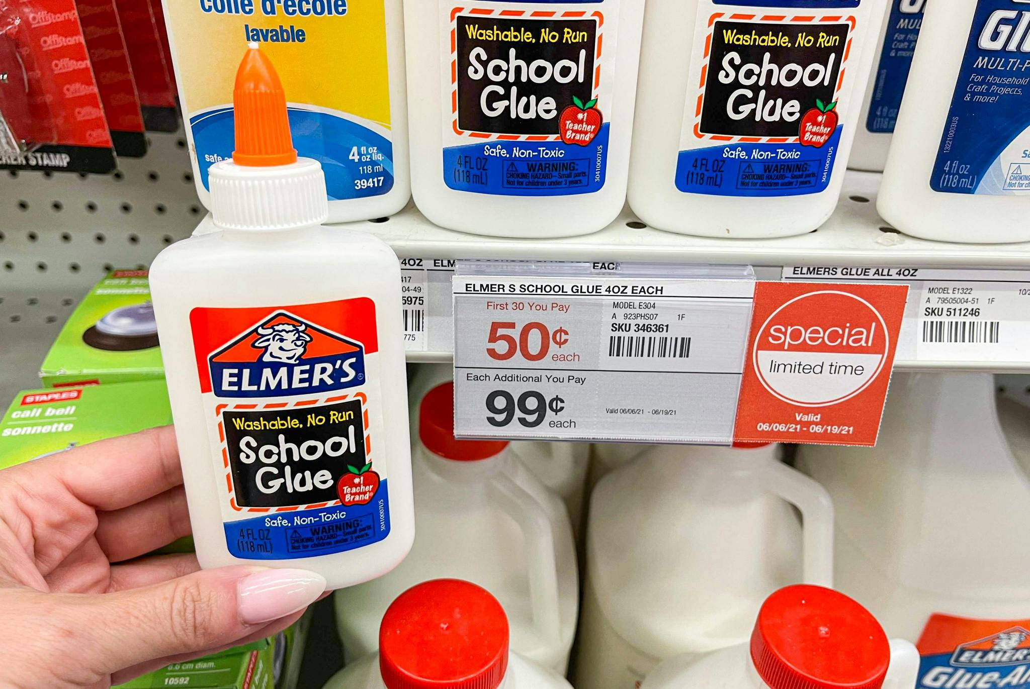 A person's hand holding a bottle of Elmer's school glue next to a shelf with a sale tag advertising a limited time offer at Staples.