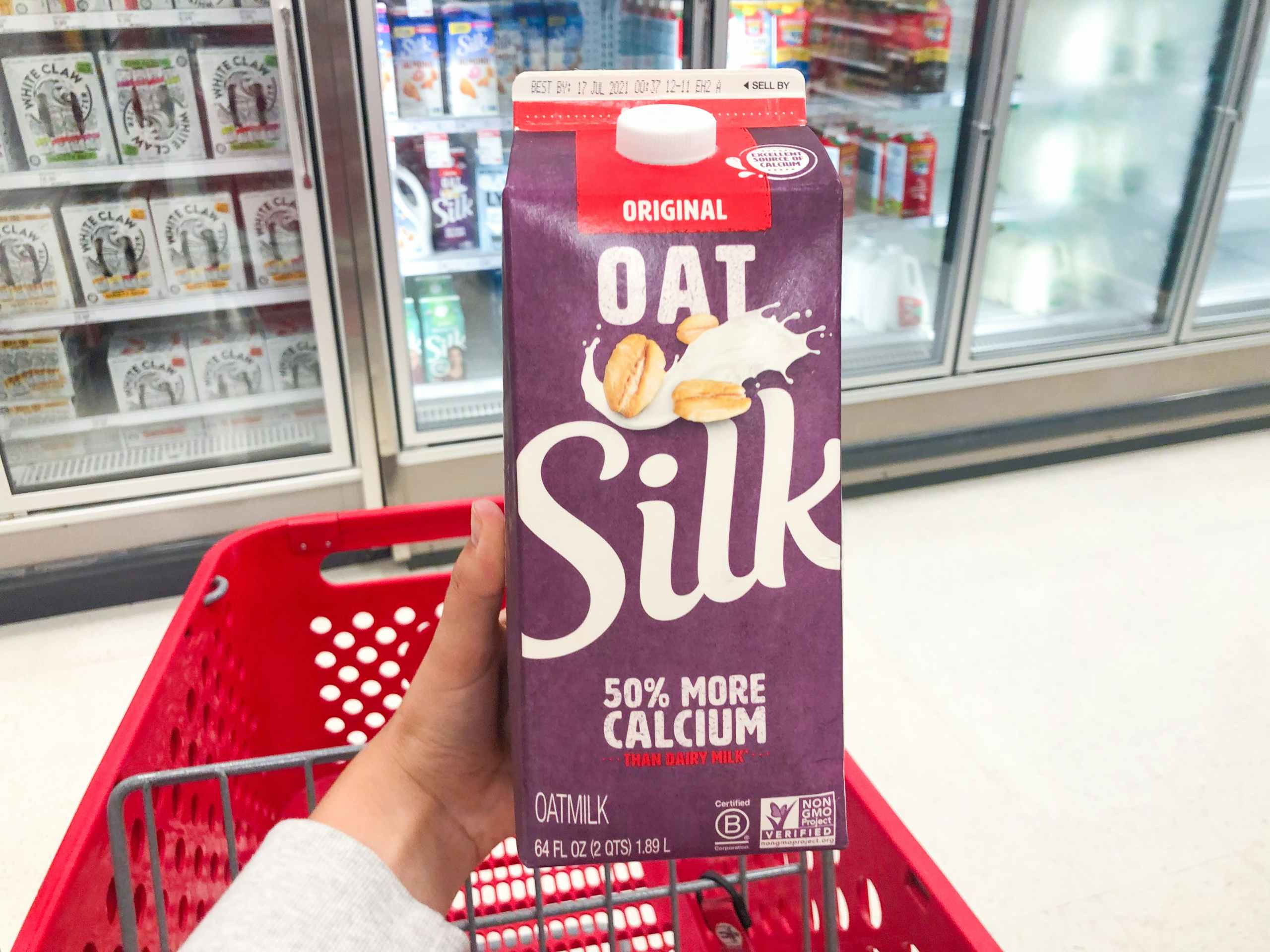 hand holding carton of oat milk above a shopping cart