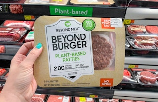 beyond burger patties held in front of meat section shelves with green sign indicating plant based meat