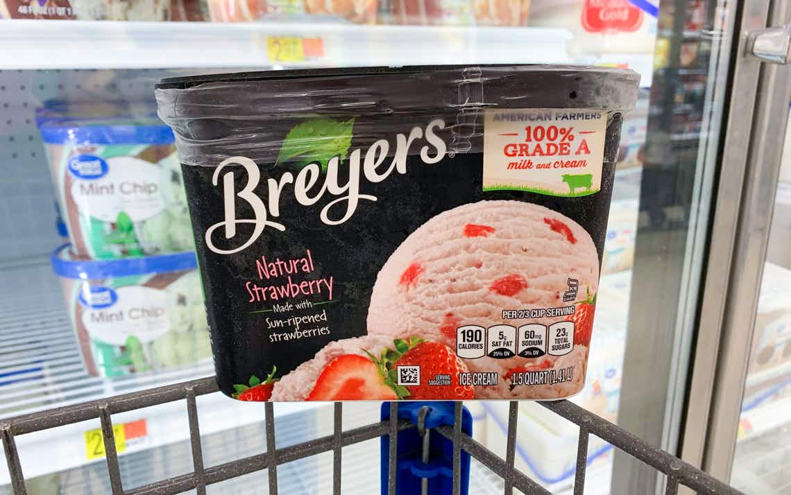 container of breyers strawberry ice cream on corner of walmart cart in front of frozen section in store