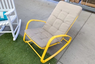 yellow metal rocking chair with tan cushion sitting in walmart garden center