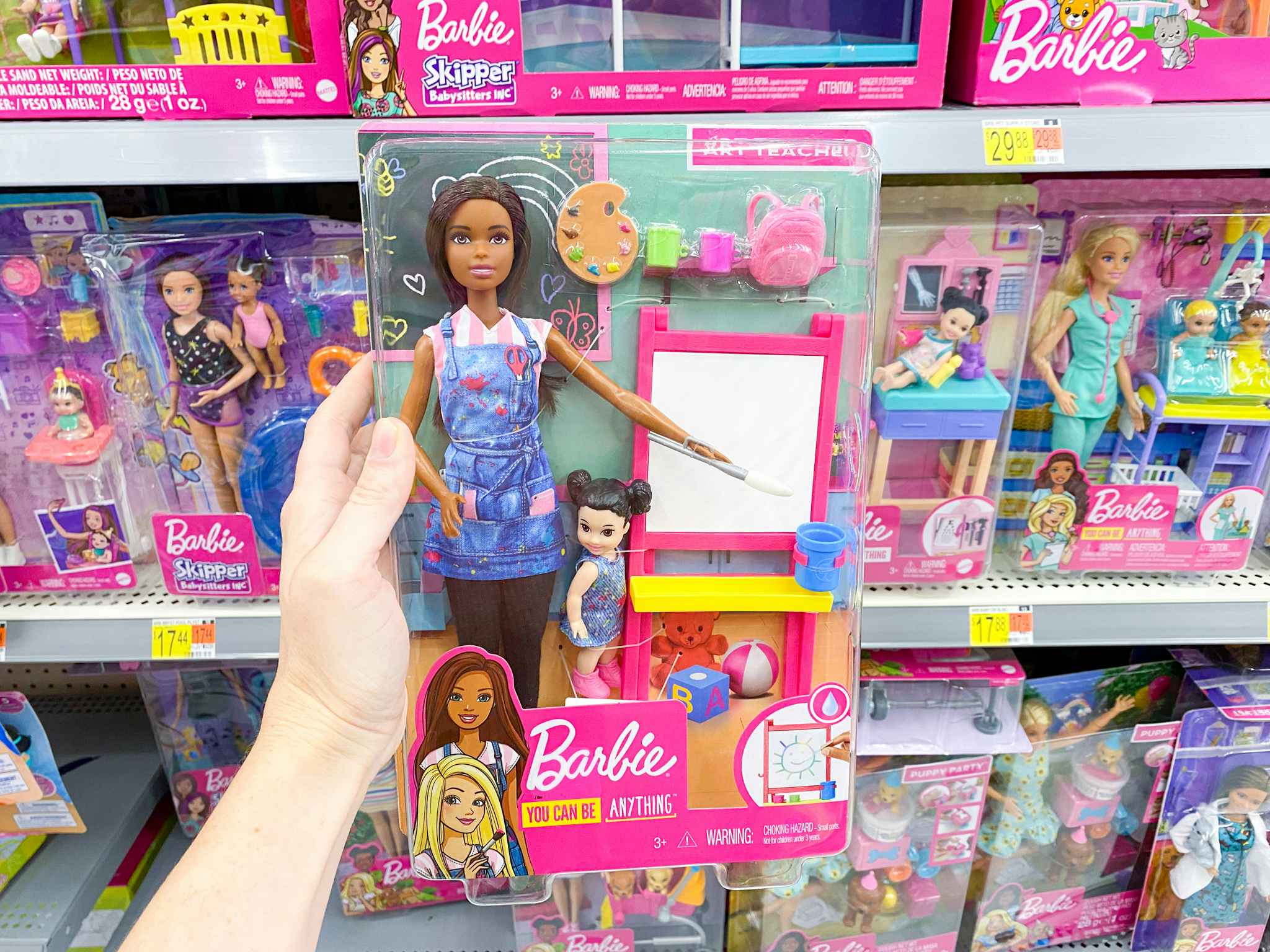 barbie art teacher set held in front of barbie shelves