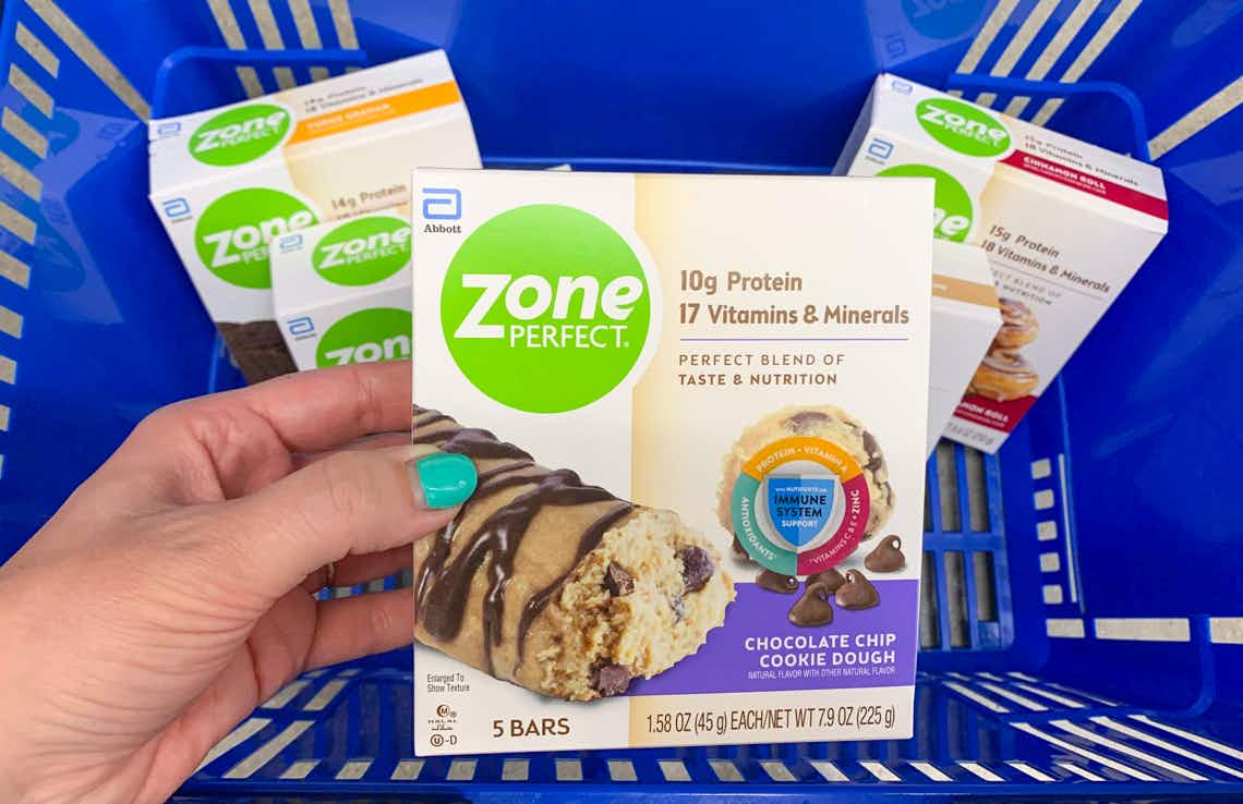 five boxes of zone perfect bars in a blue walmart hand basket wit hone box being held above the rest