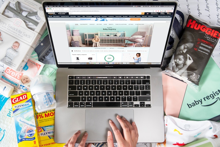 A person on Amazon.com baby registry with baby products surrounding their laptop.