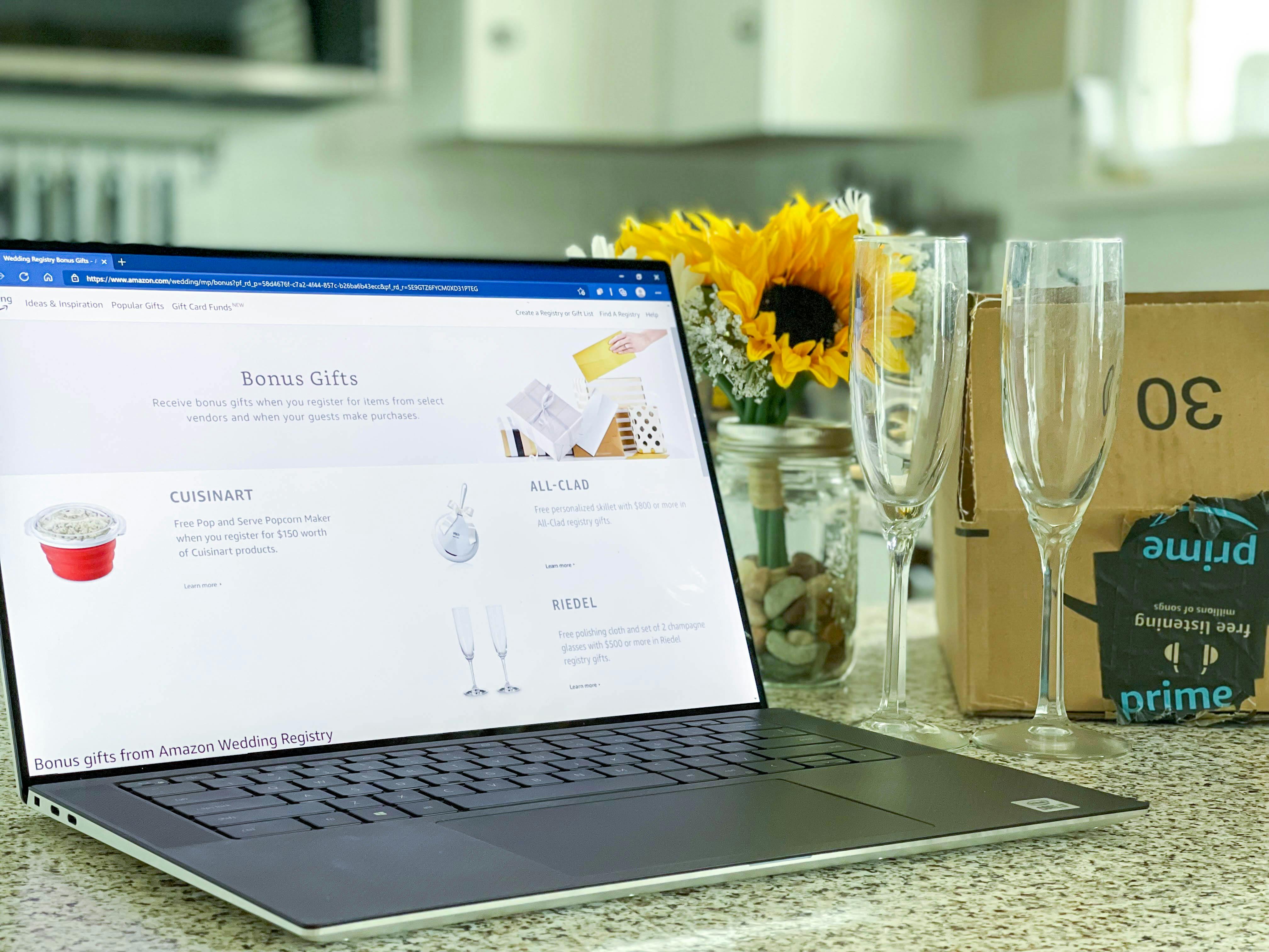 Amazon wedding registry gift page displayed on a laptop next to flowers, an Amazon box, and champagne flutes
