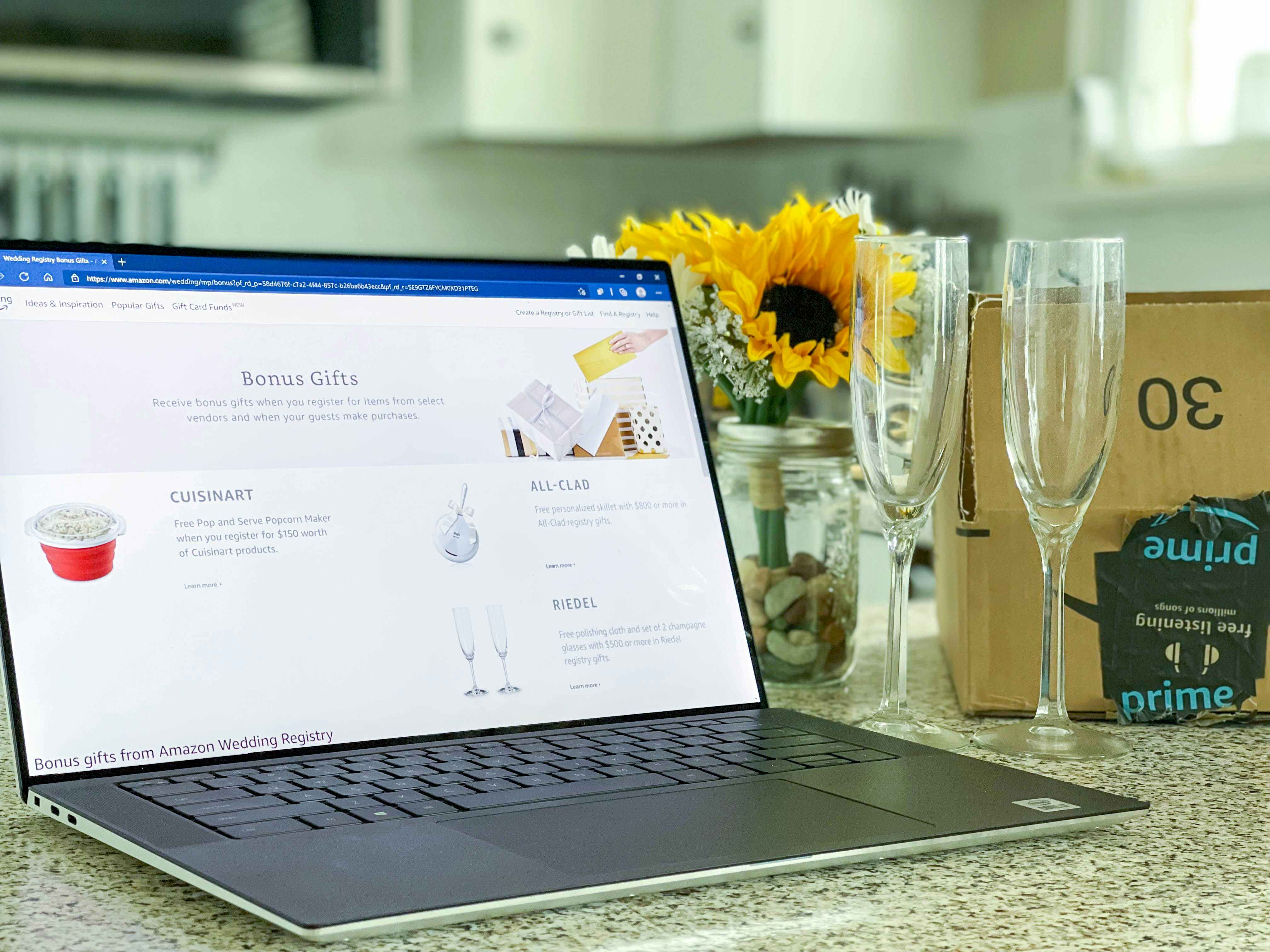 Amazon wedding registry gift page displayed on a laptop next to flowers, amazon box, and champagne flutes