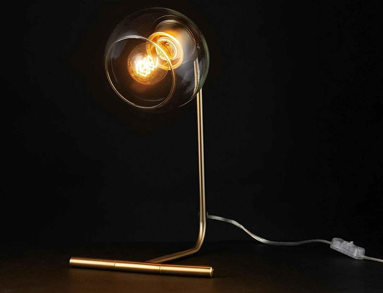 A Globe Electric desk lamp lit up in a dark area.