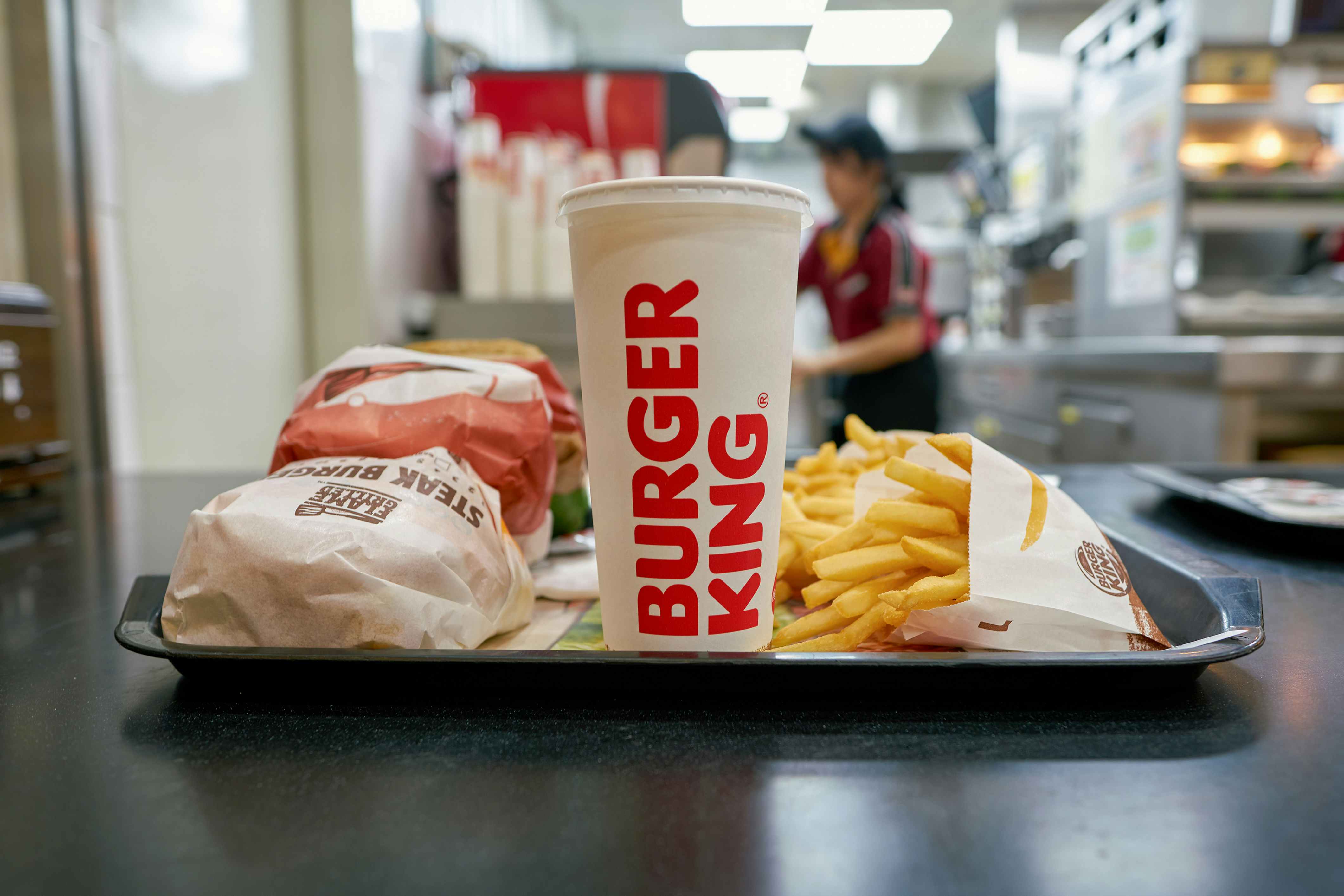 A tray sitting on the counter at Burger King with three wrapped burgers, two bags of fries, and a drink cup boldly featuring the words 