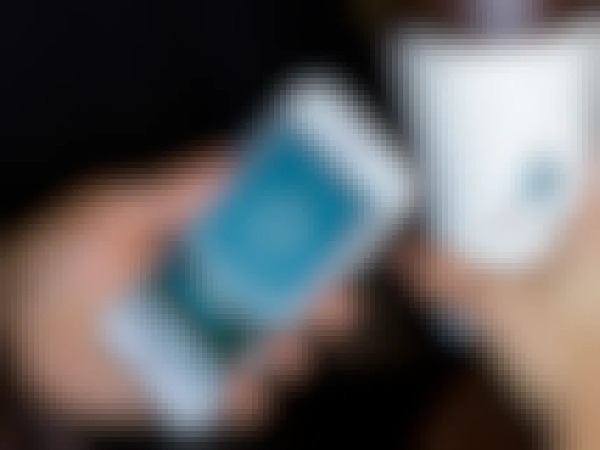 A person holding a cell phone next to a cup of coffee.