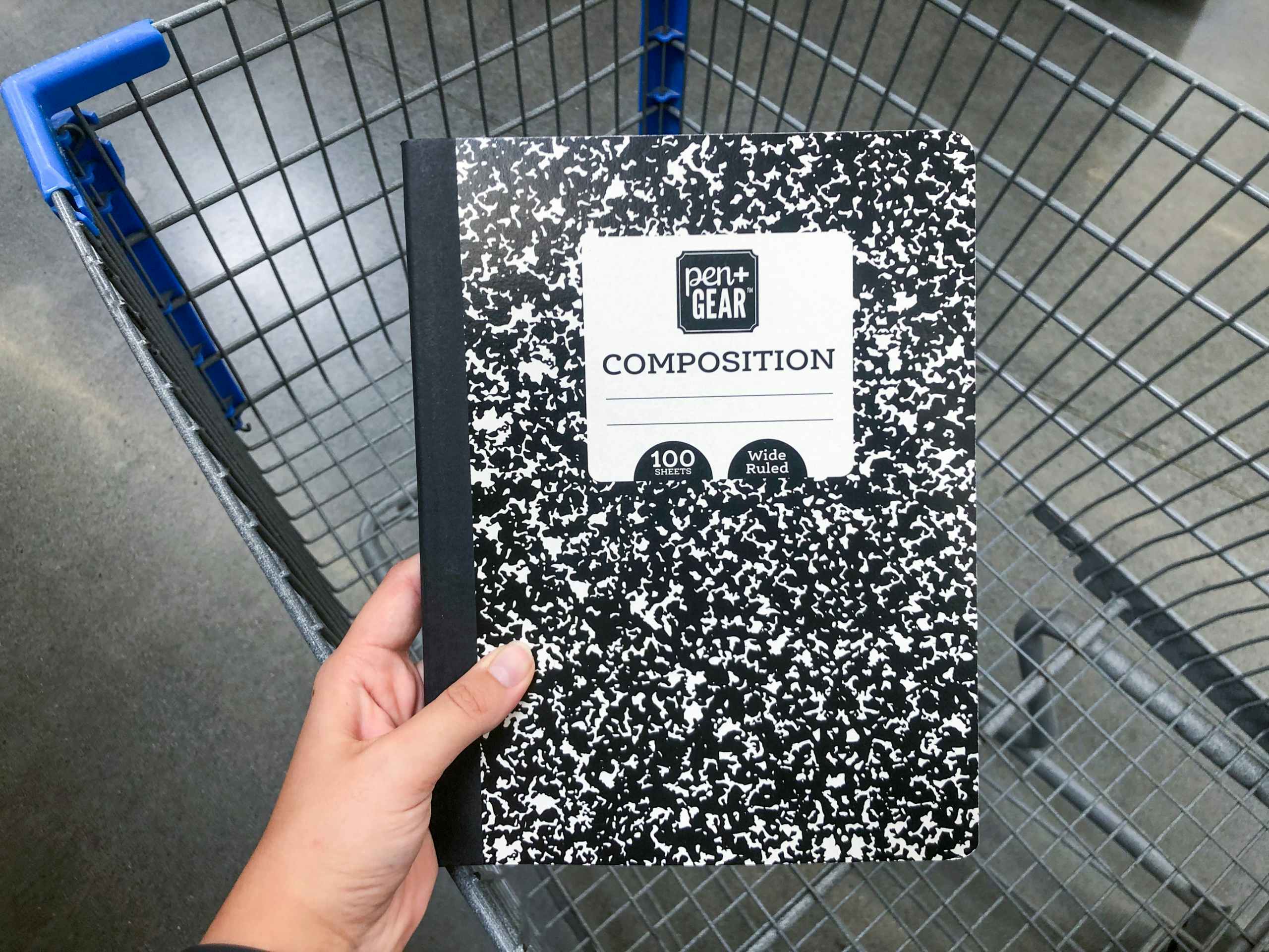 hand holding composition notebook over an empty Walmart shopping cart