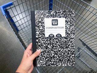 hand holding composition notebook over an empty Walmart shopping cart