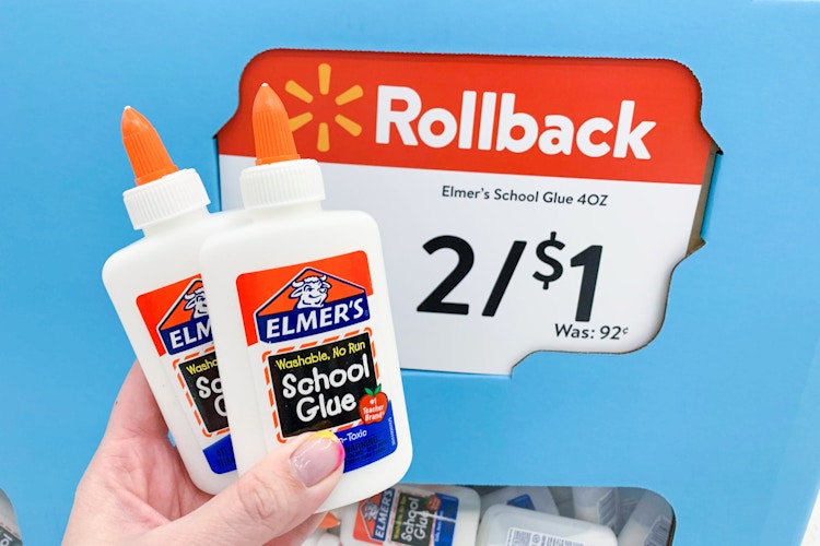 A person's hand holding 2 bottles of Elmer's School Glue in front of a Walmart Rollback sale sign that reads, "Elmer's school glue 4oz, 2/$1" inside Walmart.