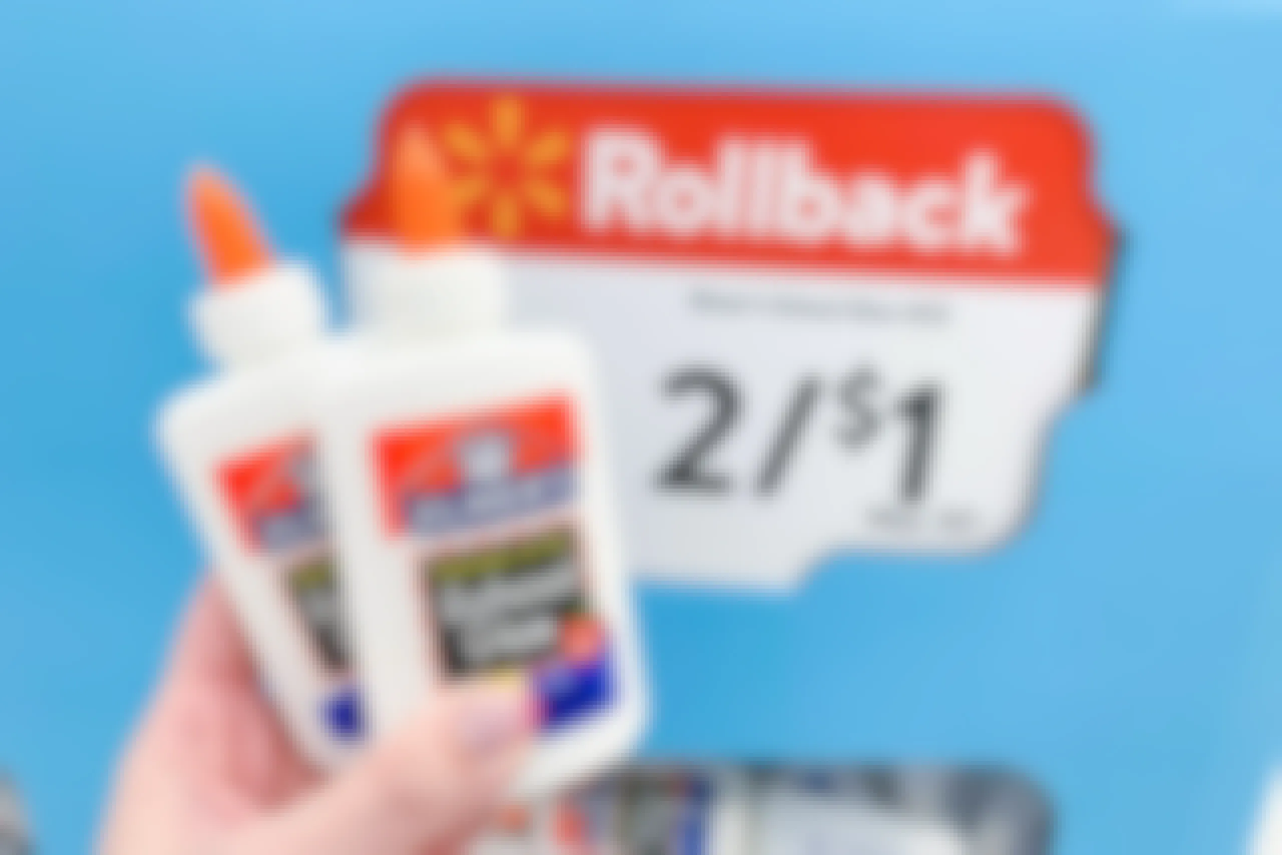 A person's hand holding 2 bottles of Elmer's School Glue in front of a Walmart Rollback sale sign that reads, "Elmer's school glue 4oz, 2/$1" inside Walmart.