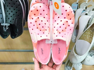 hand holding a pair of toddler water shoes with one hand on the shoe display at Target