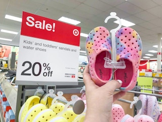 hand holding a pair of toddler water shoes in front of shoe display sale sign at Target