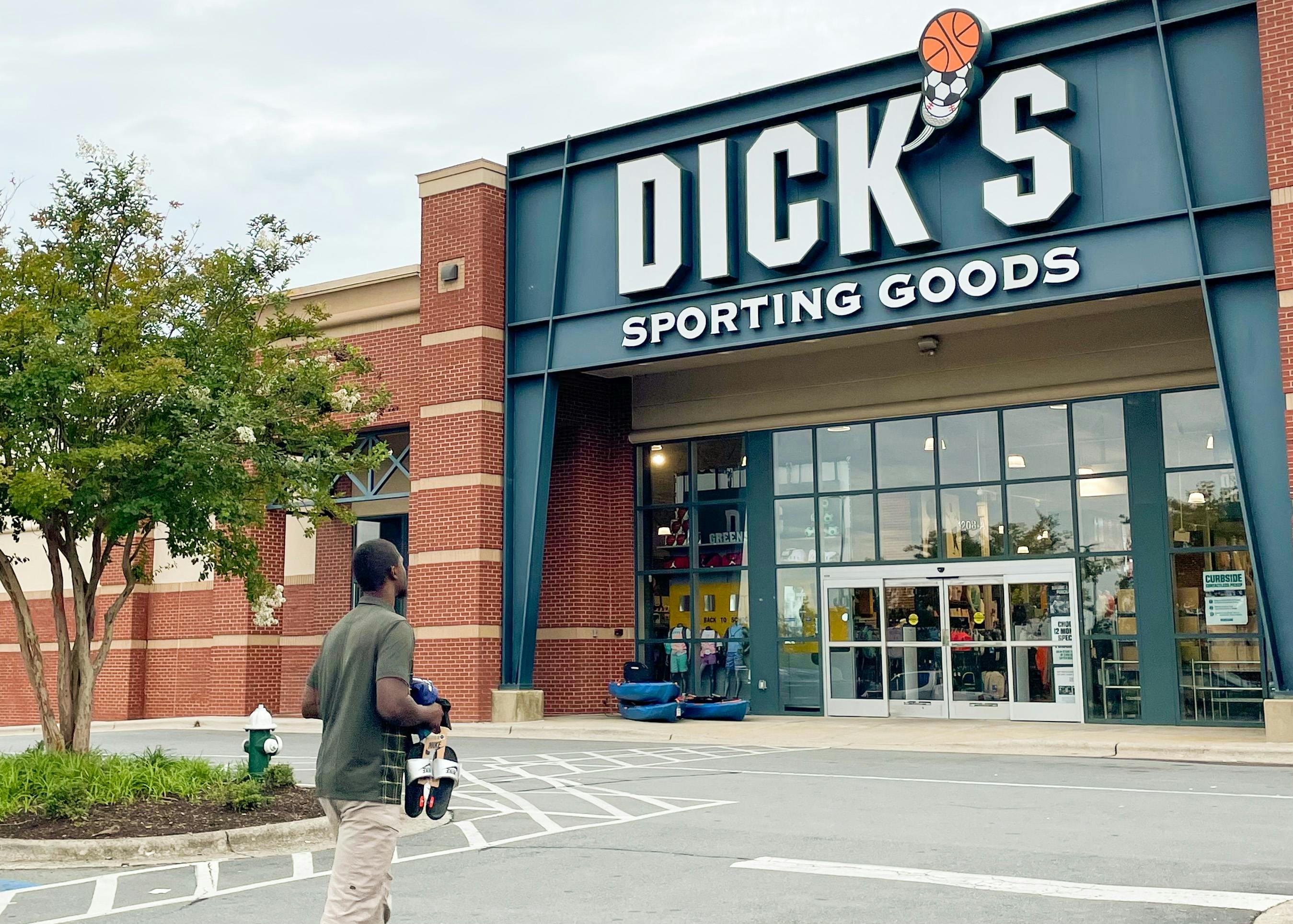 A man walking into Dick's Sporting Goods with items in hand