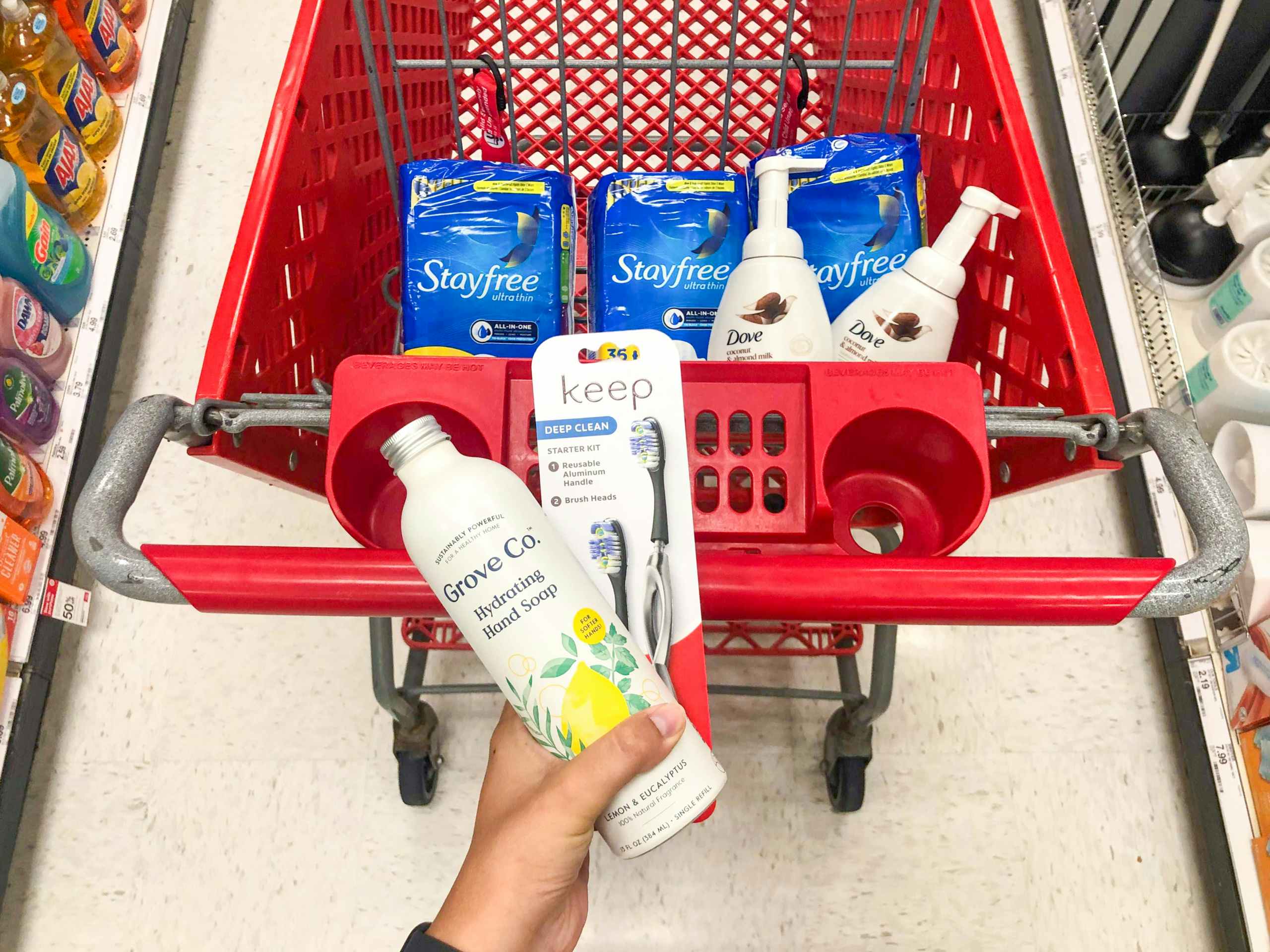 hand holding soap and toothbrush in front of shopping cart
