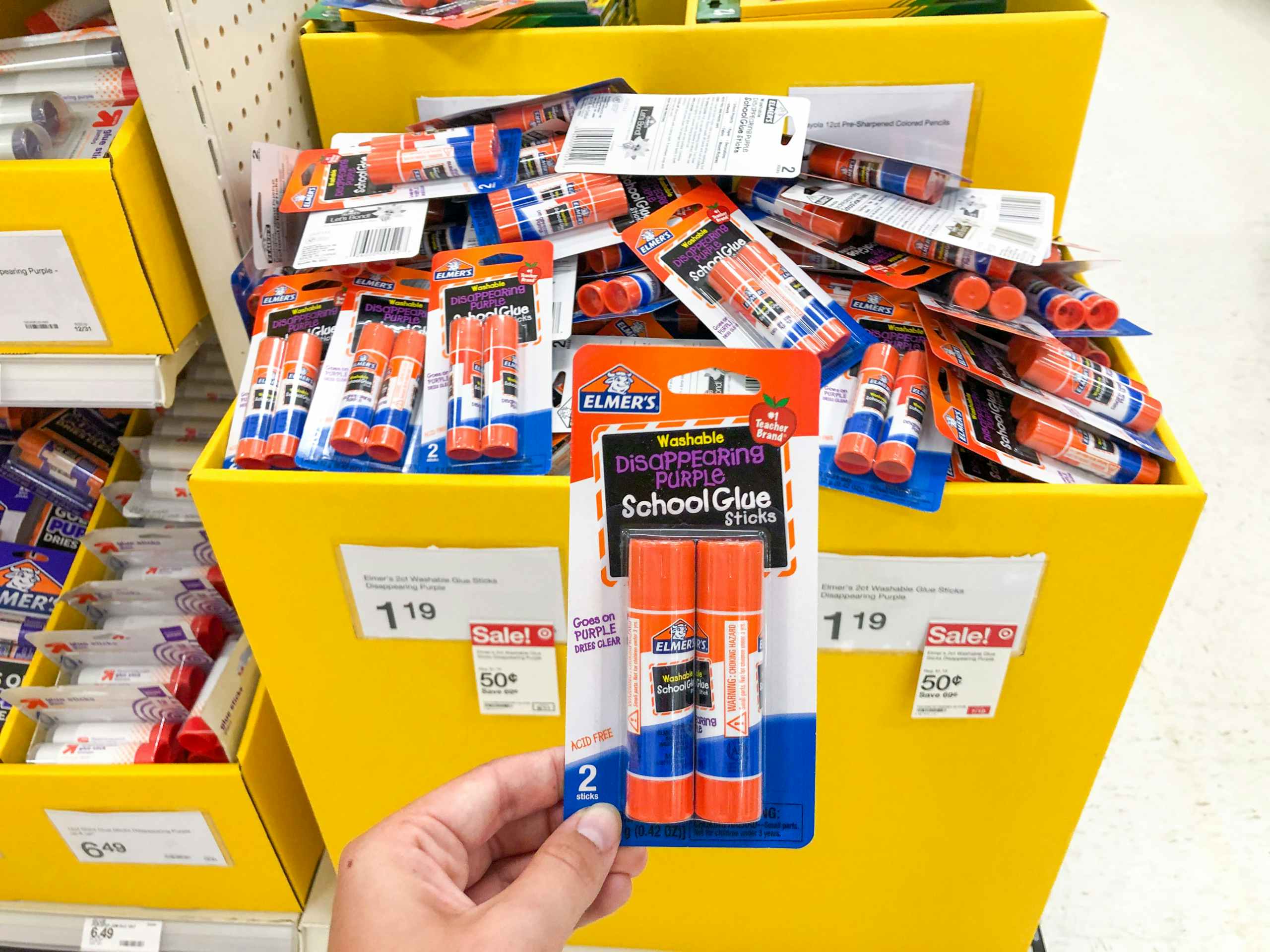 hand holding one package of glue sticks in front of $0.50 sale sign