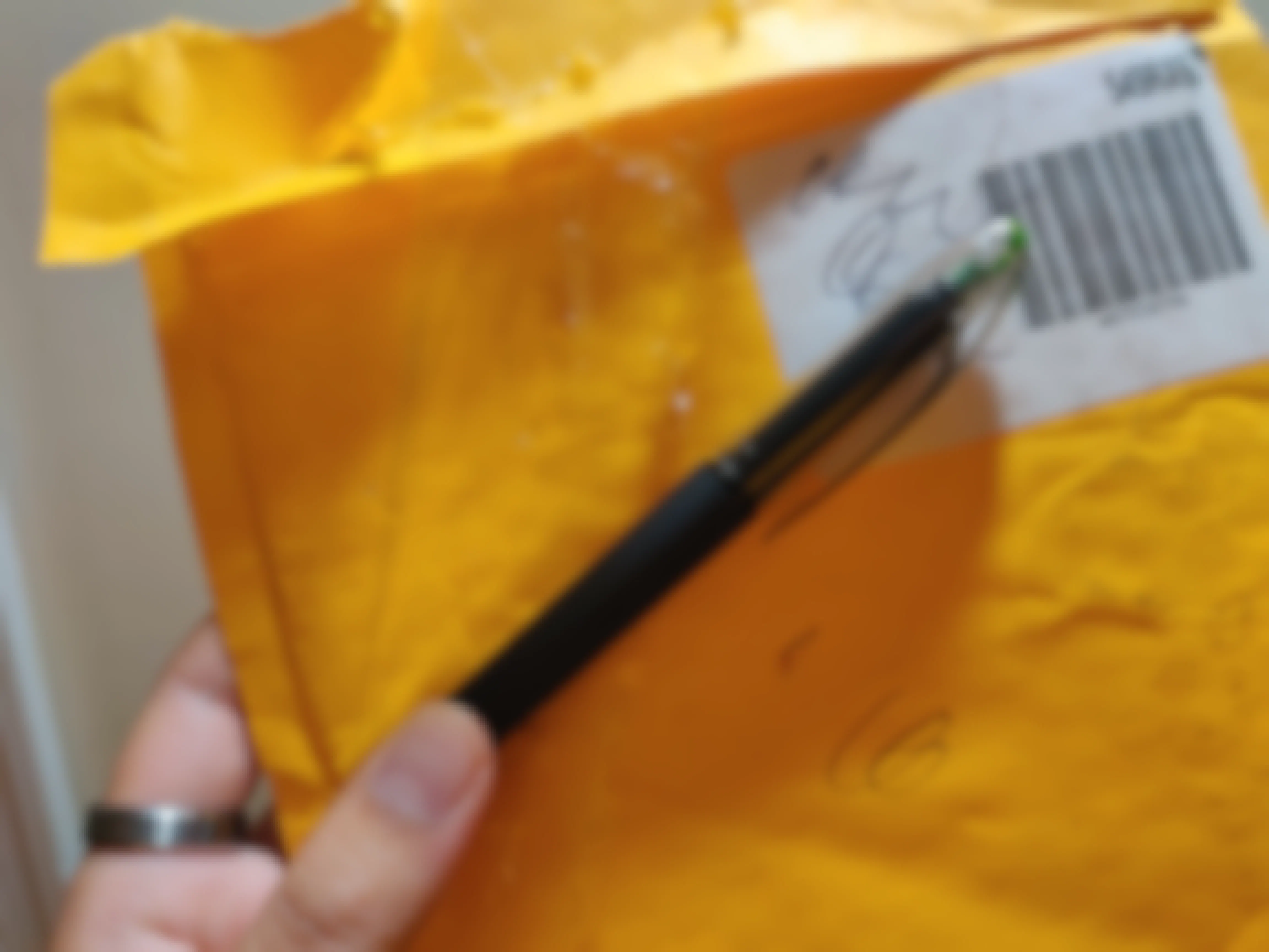 A person's hand holding a pen and a shipping envelope with scribble marks on it.