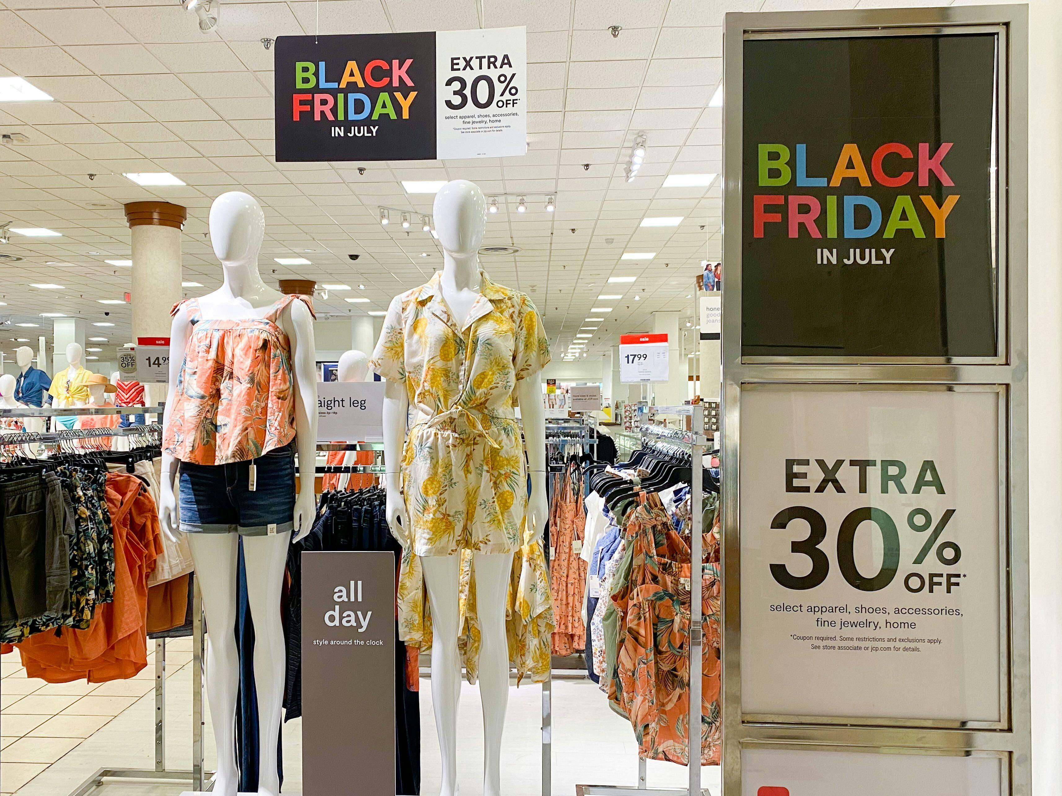 JCPenney Black Friday in July Sale signs at the front of the store next to some mannequins dressed in summer clothing.