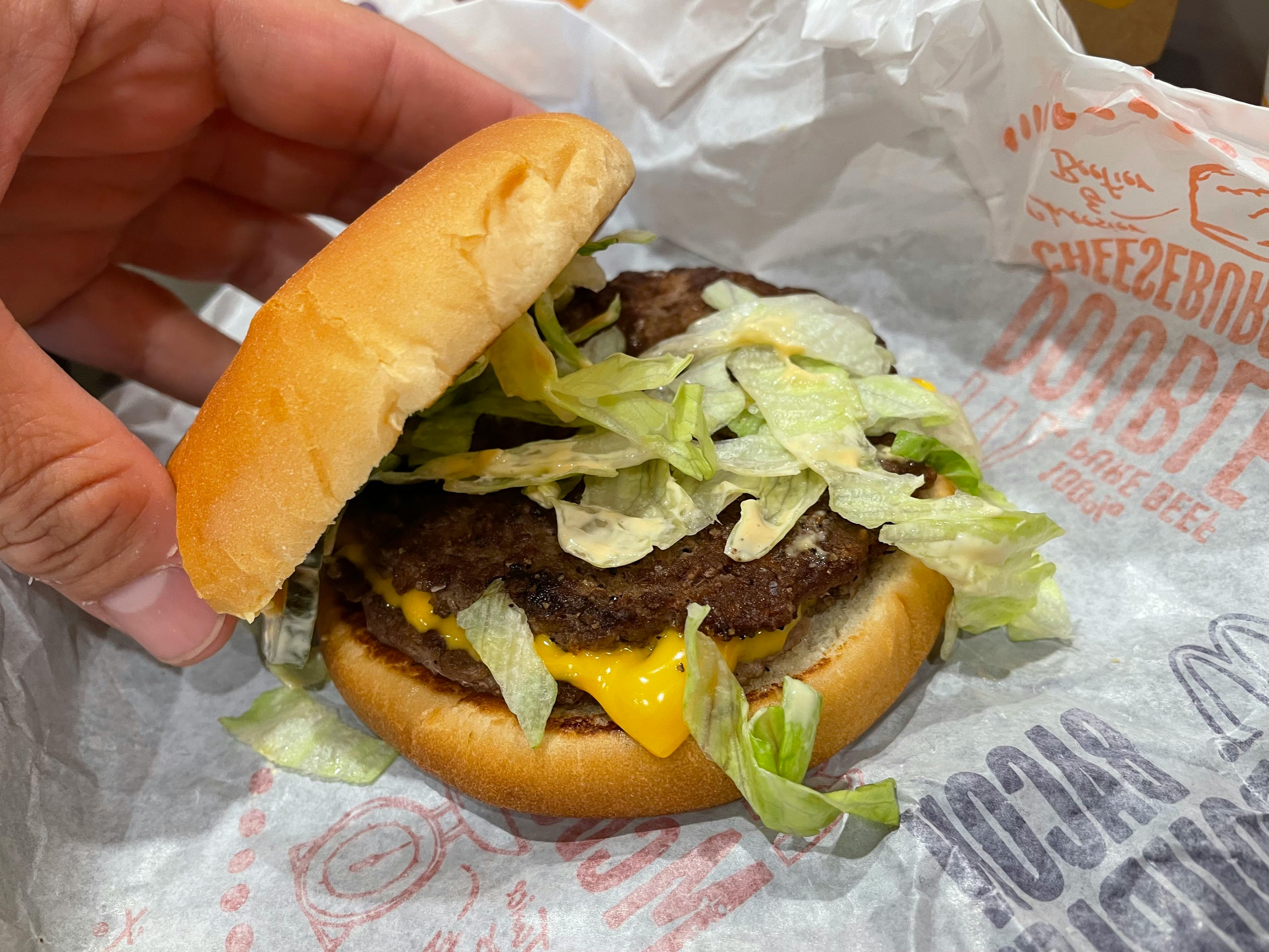 A person's hand lifting the top bun off of a McDonald's burger sitting on its paper wrapping.