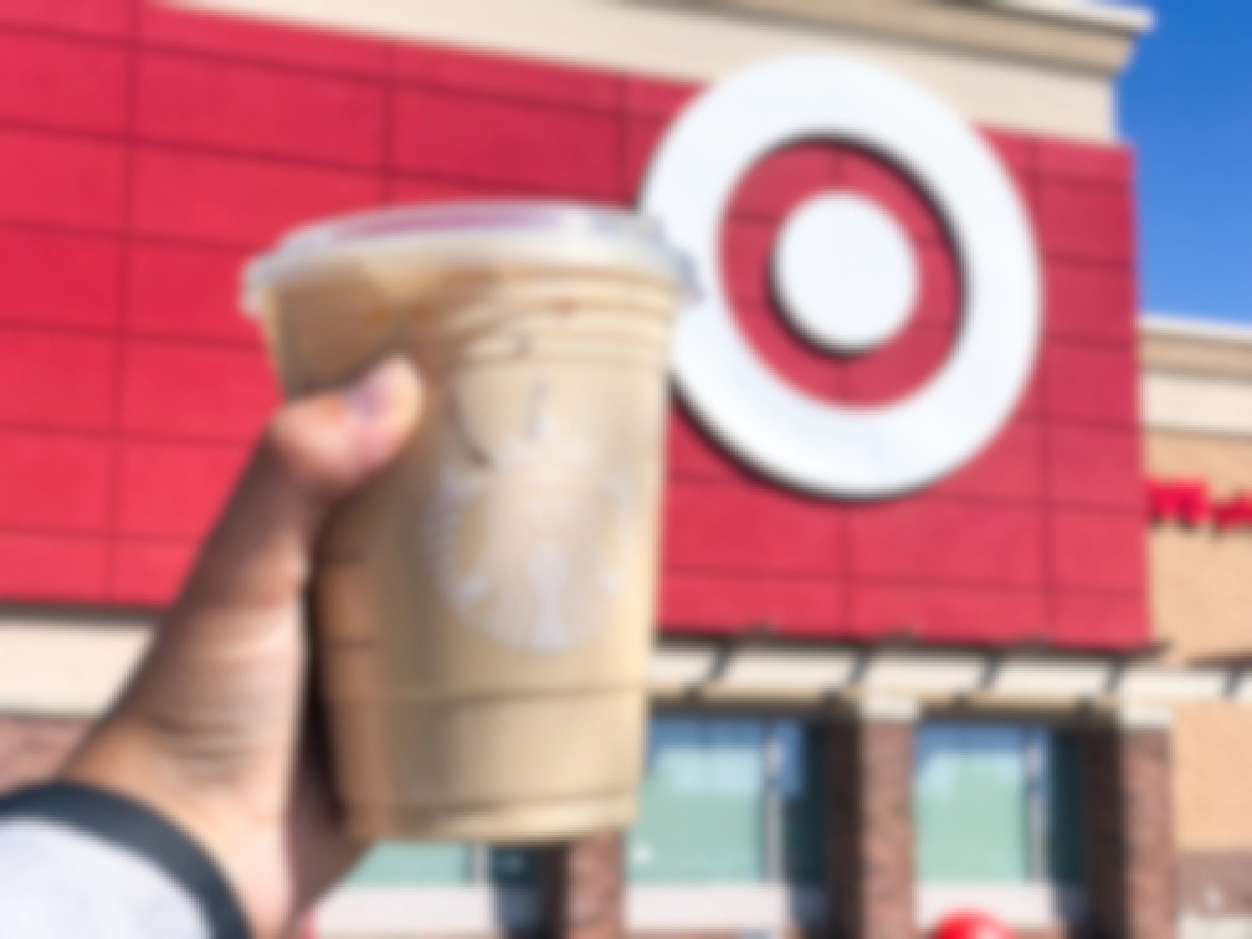 A person's hand holding up a Starbucks iced coffee in front of a Target storefront.