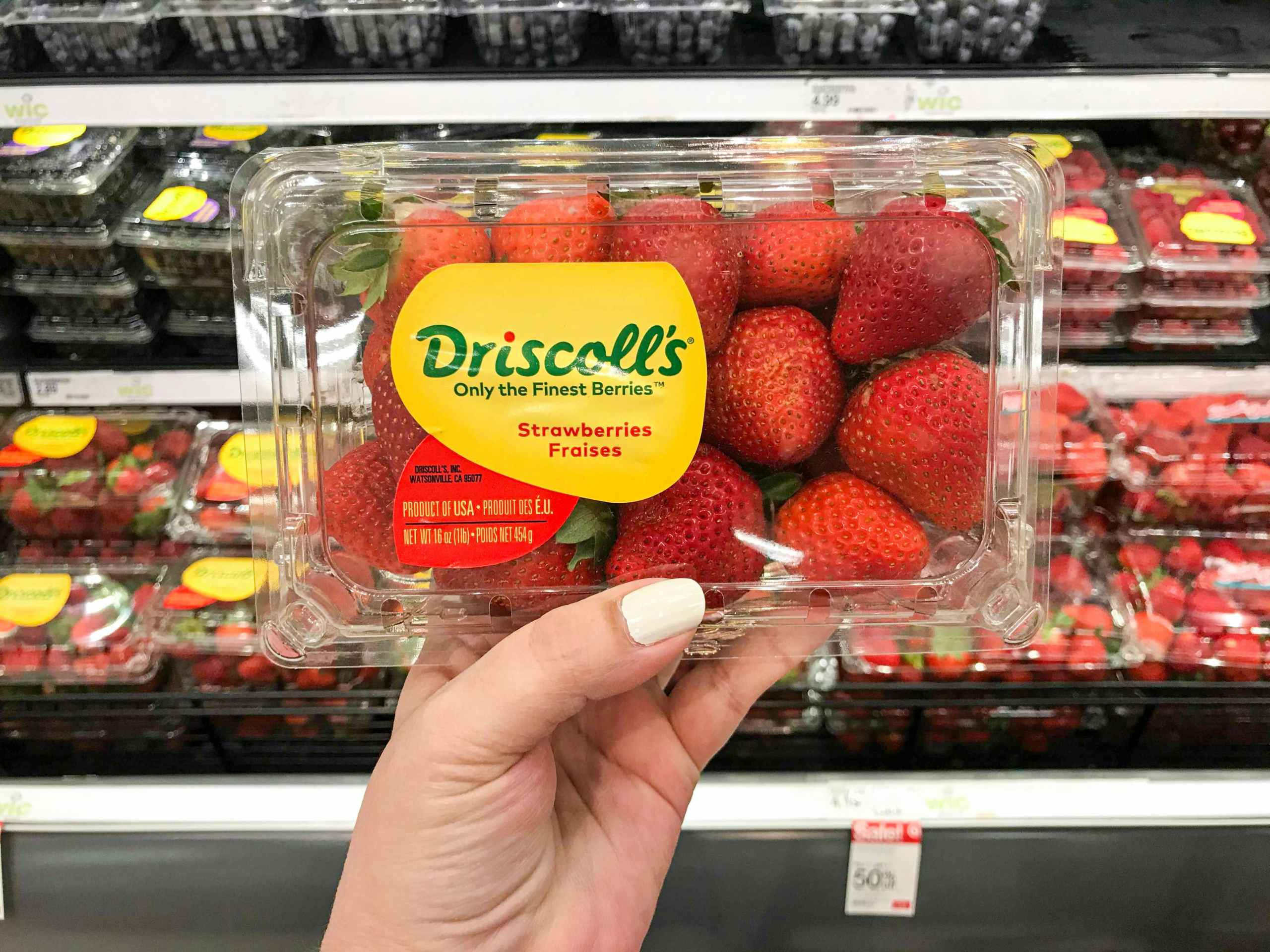 hand holding 1-pound package of fresh strawberries in front of produce aisle at Target