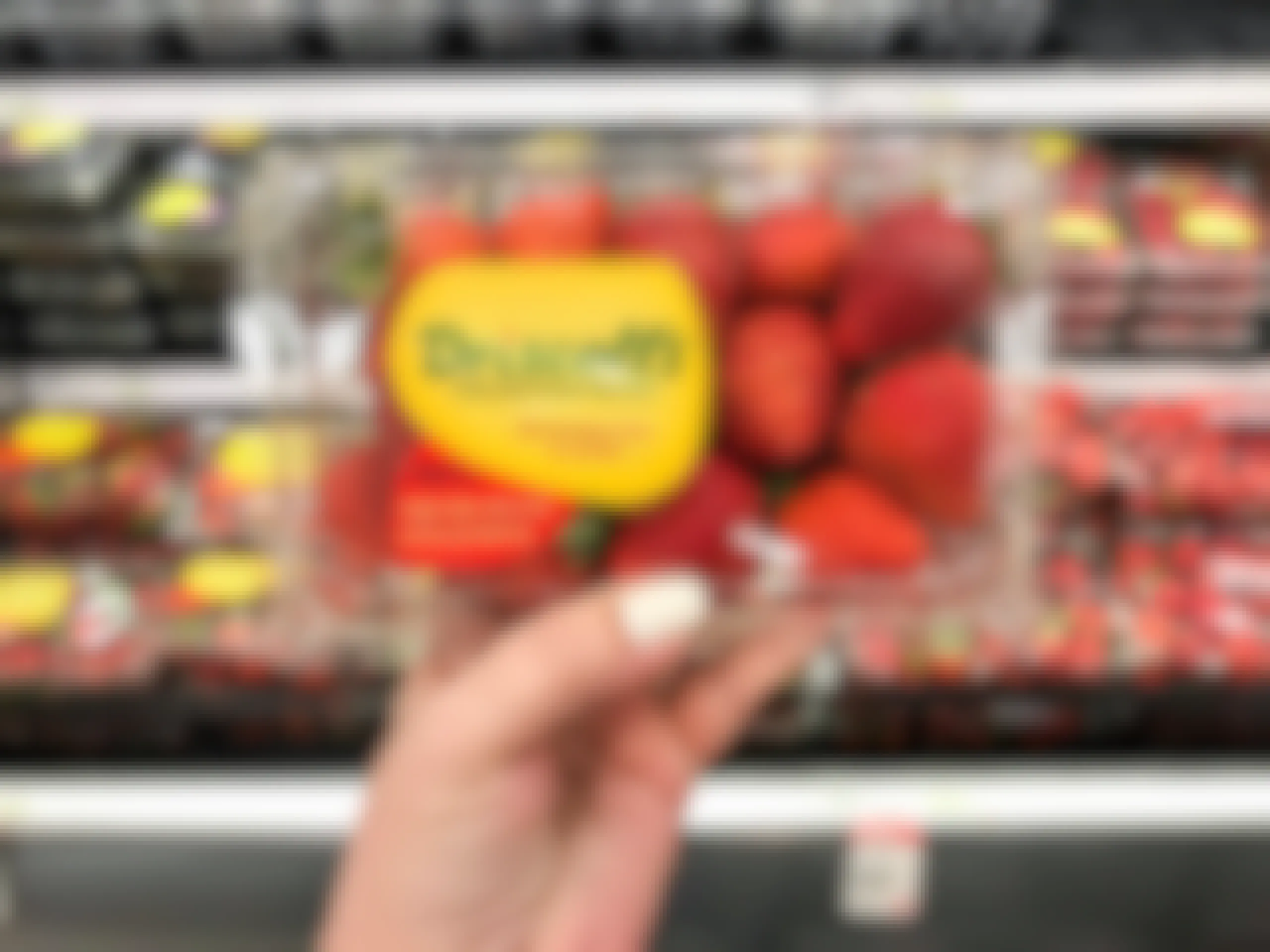 hand holding 1-pound package of fresh strawberries in front of produce aisle at Target