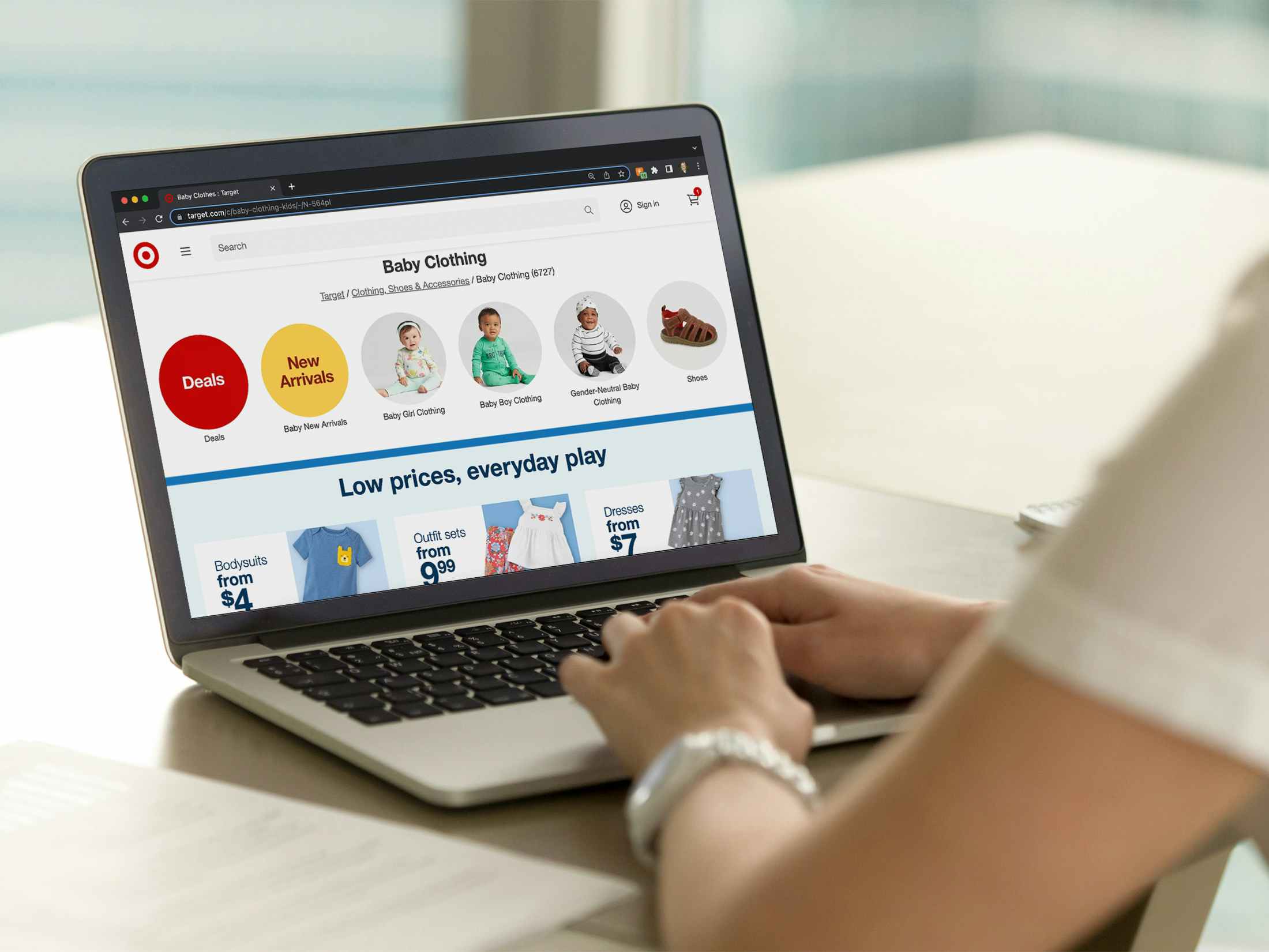 A person using a laptop, looking at the Baby Clothing section on Target's website.