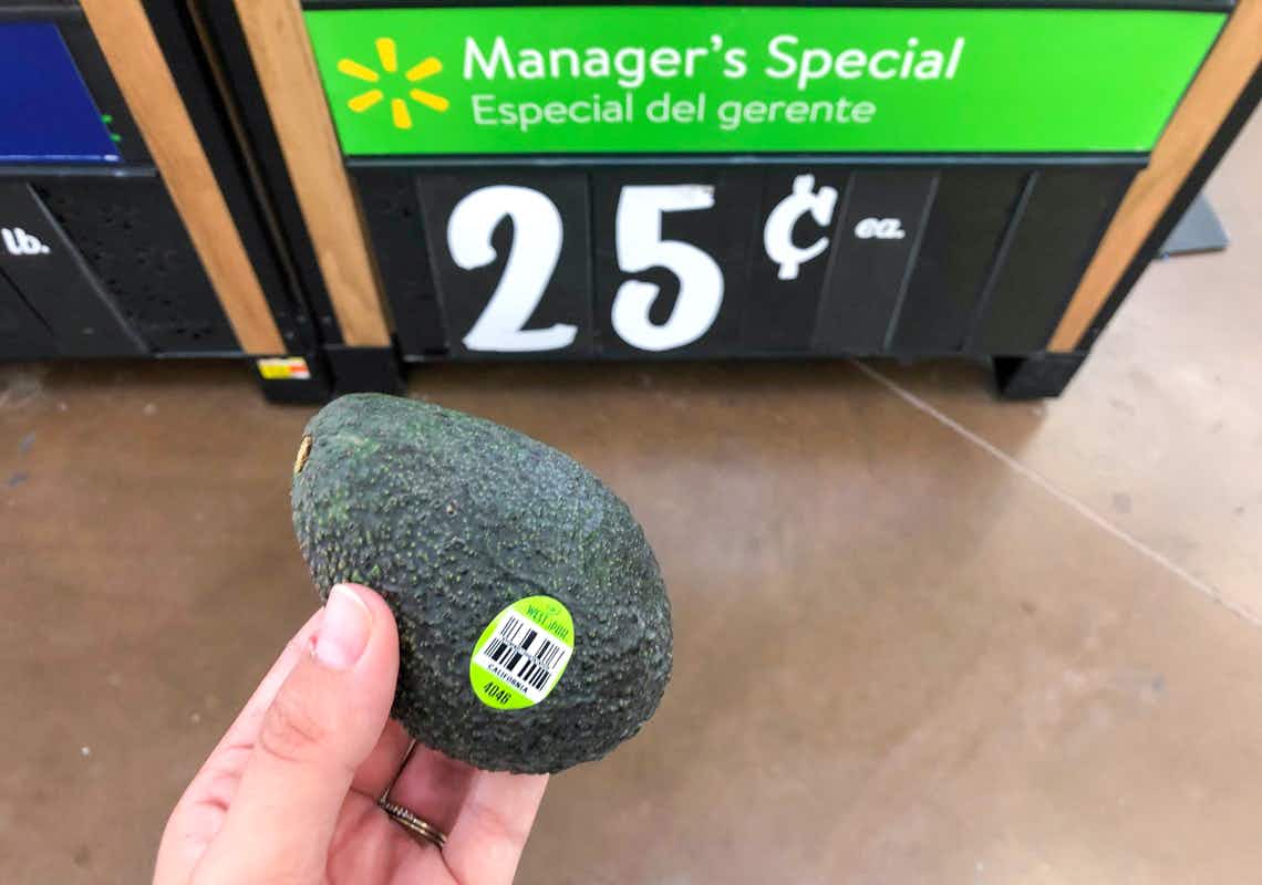 small avocado held by hand in front of manager's special sign on avocado bin at walmart