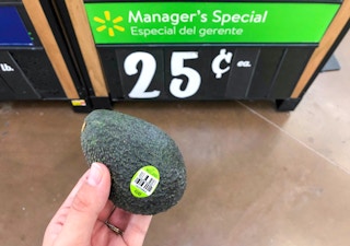 small avocado held by hand in front of manager's special sign on avocado bin at walmart