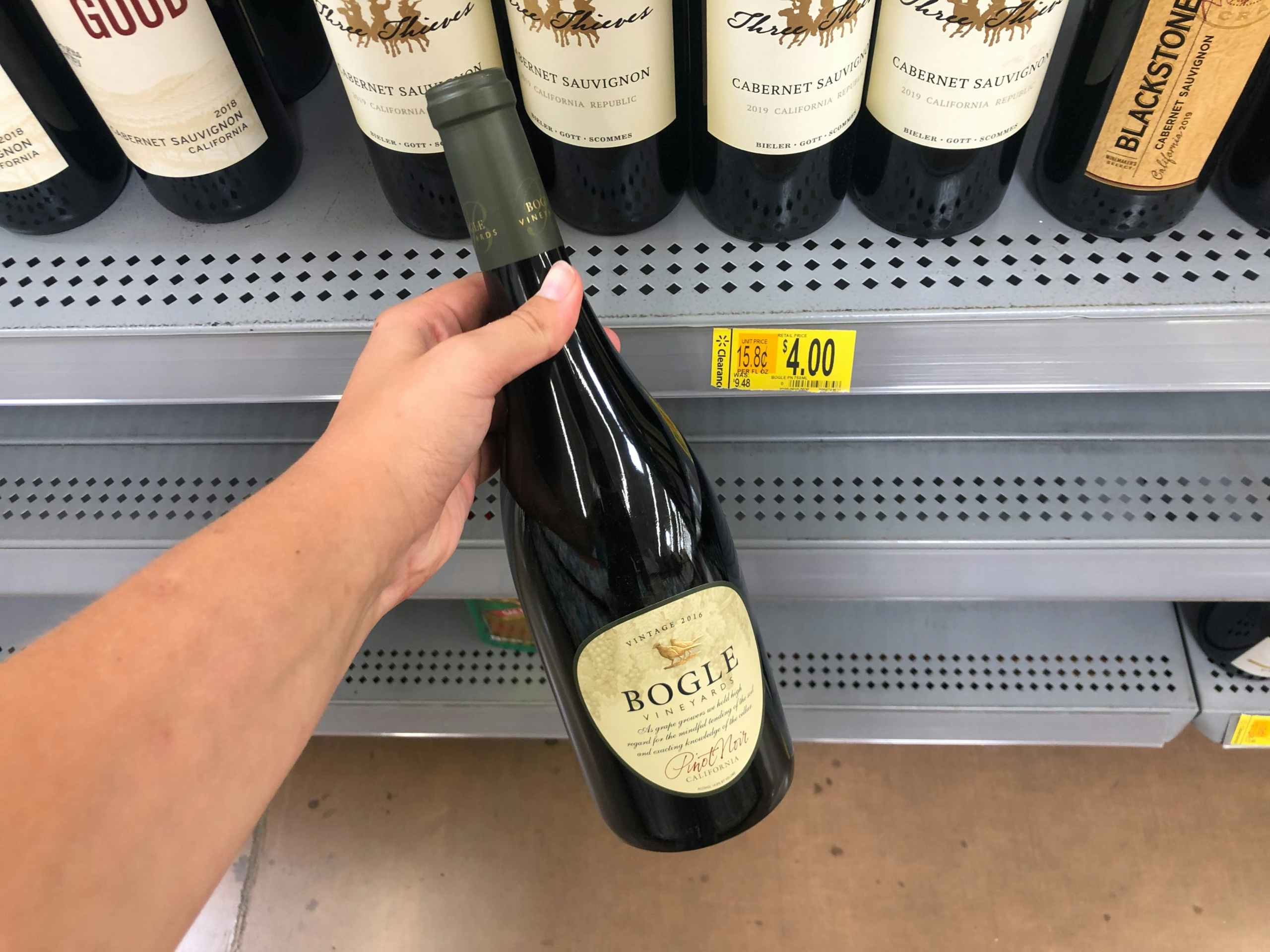 hand holding bottle of wine in front of clearance display at Walmart