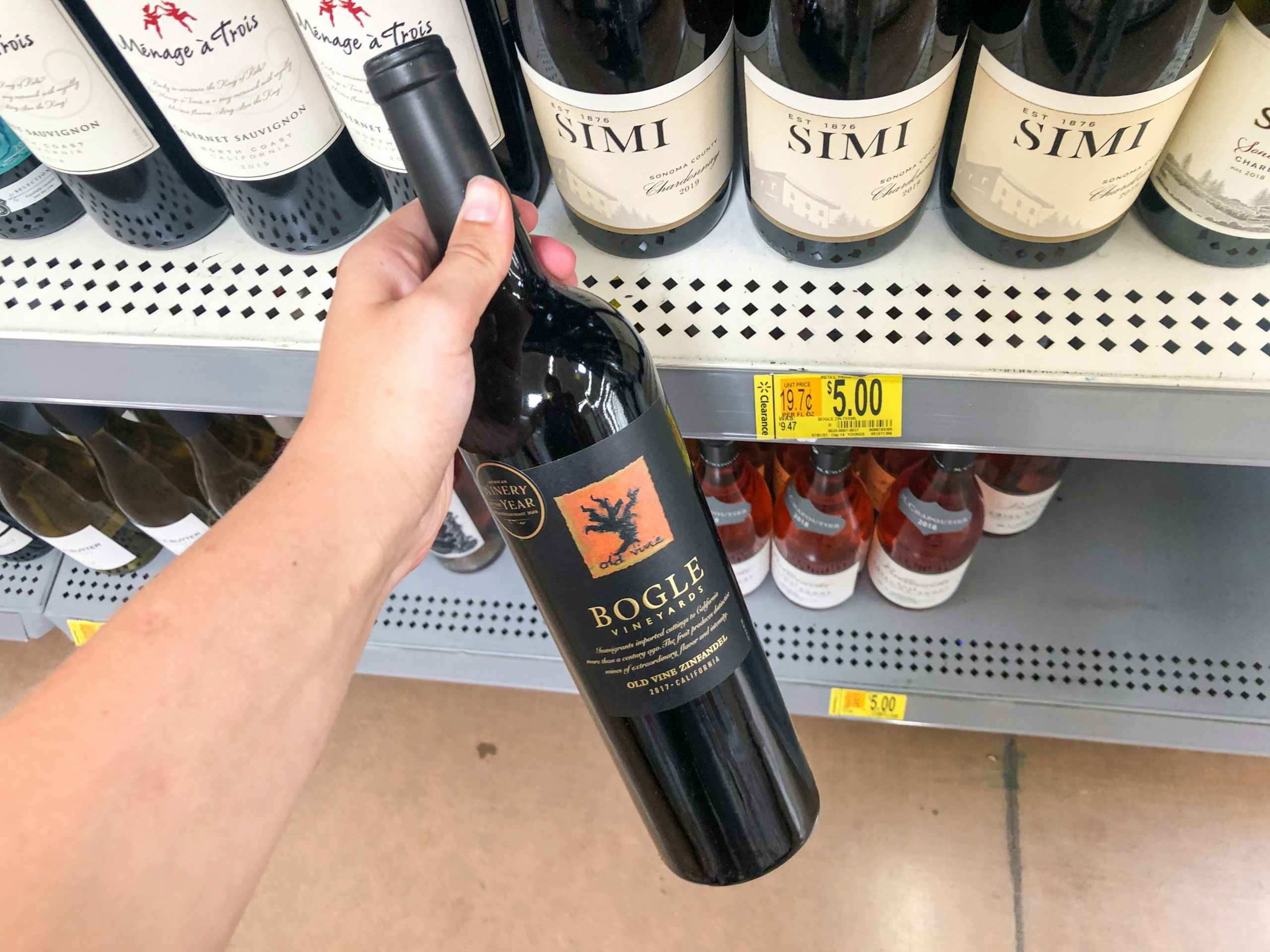 hand holding bottle of wine in front of clearance display at Walmart