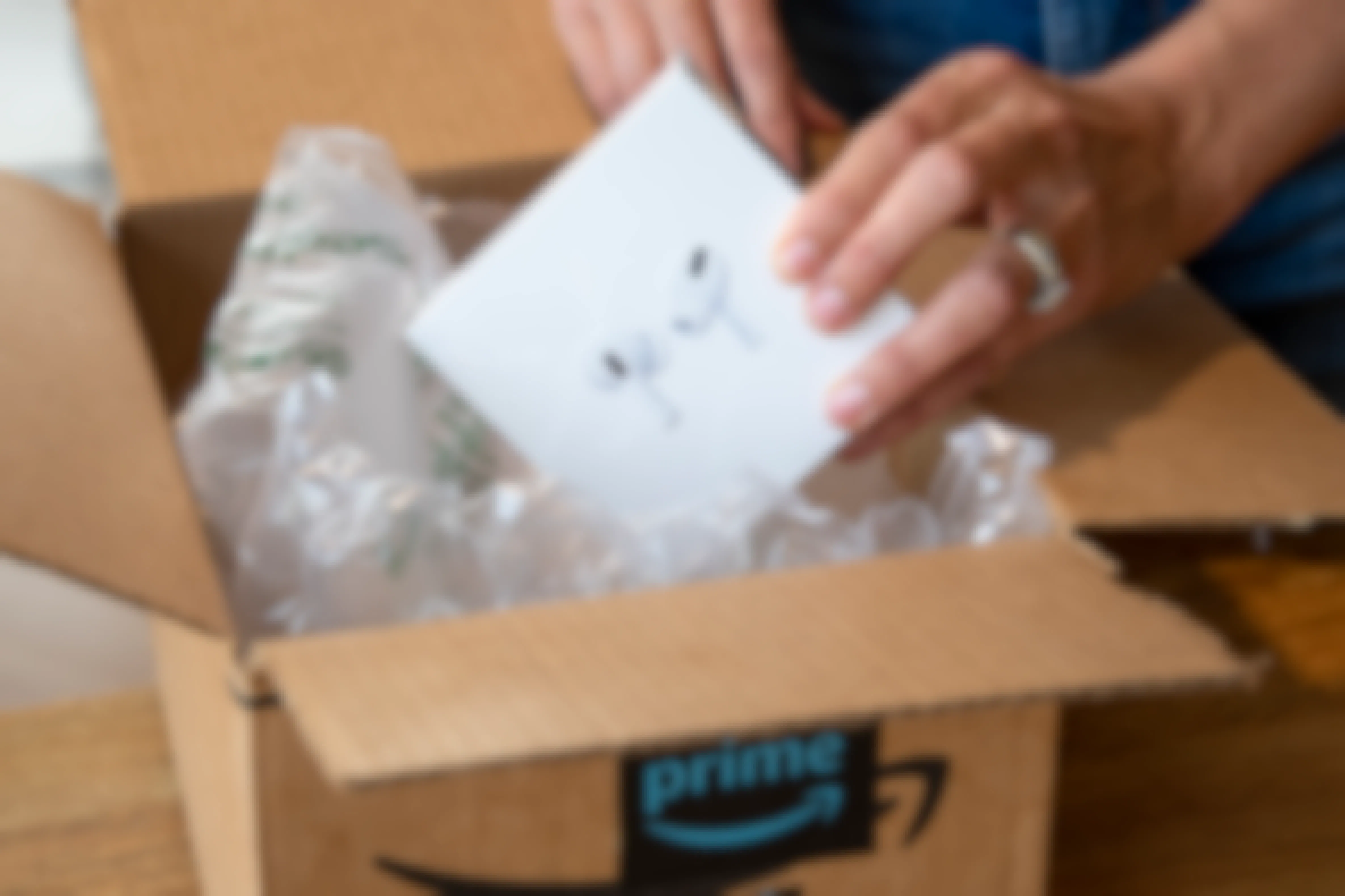 A person pulling a box of Apple Airpod pros out of an Amazon box.
