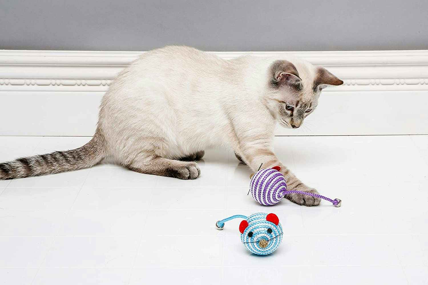 A cat playing with two bell mouse toys.