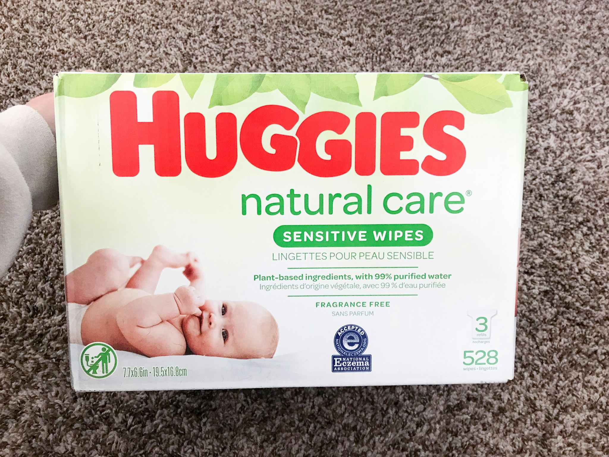A hand holding a box of Huggies Natural Care Sensitive Baby Wipes.