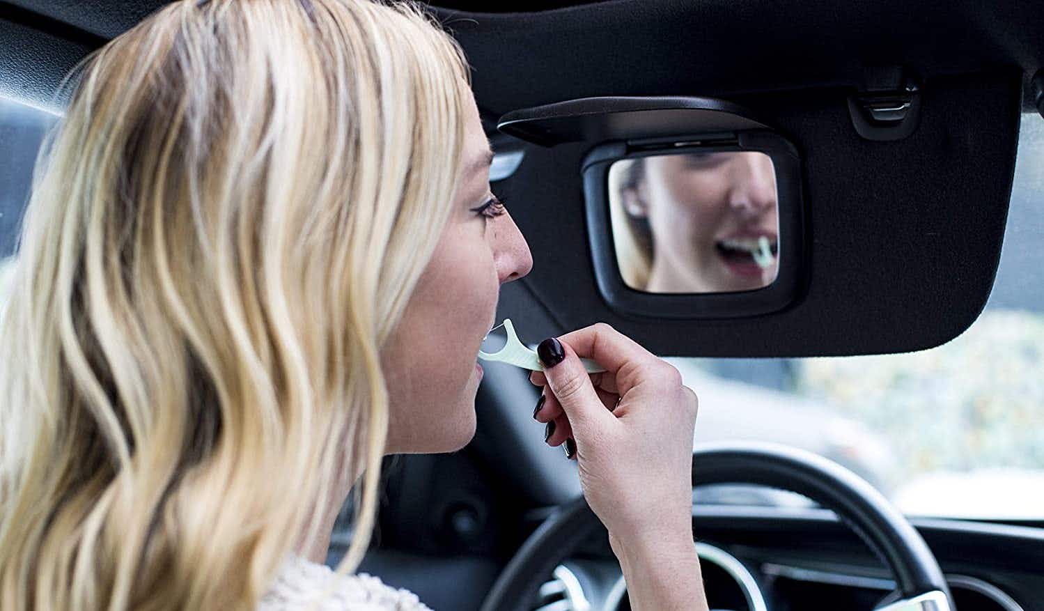 A woman using a Plackers dental floss pick in her car.