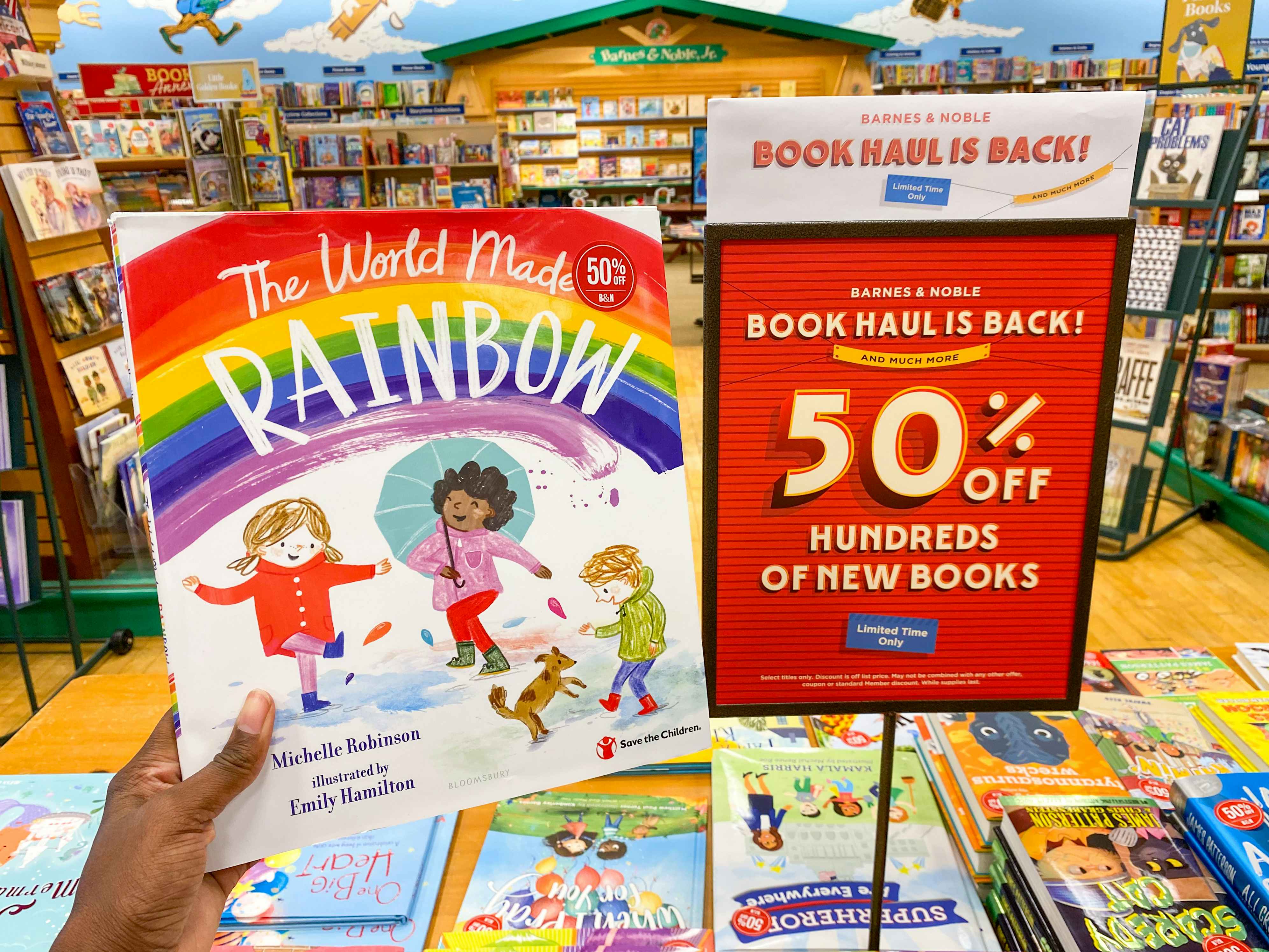 someone holding up a children's book next to a sale sign reading 50 percent off with a row of books below, in the middle of barnes and noble