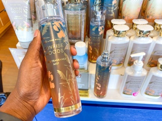 a person holding a body mist spray in front of a display in bath and body works