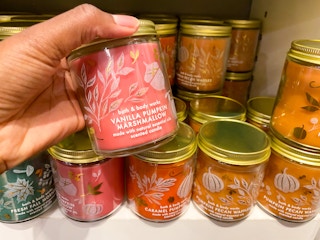 a person picking up a fall scented candle with a display of candles behind in bath and body works